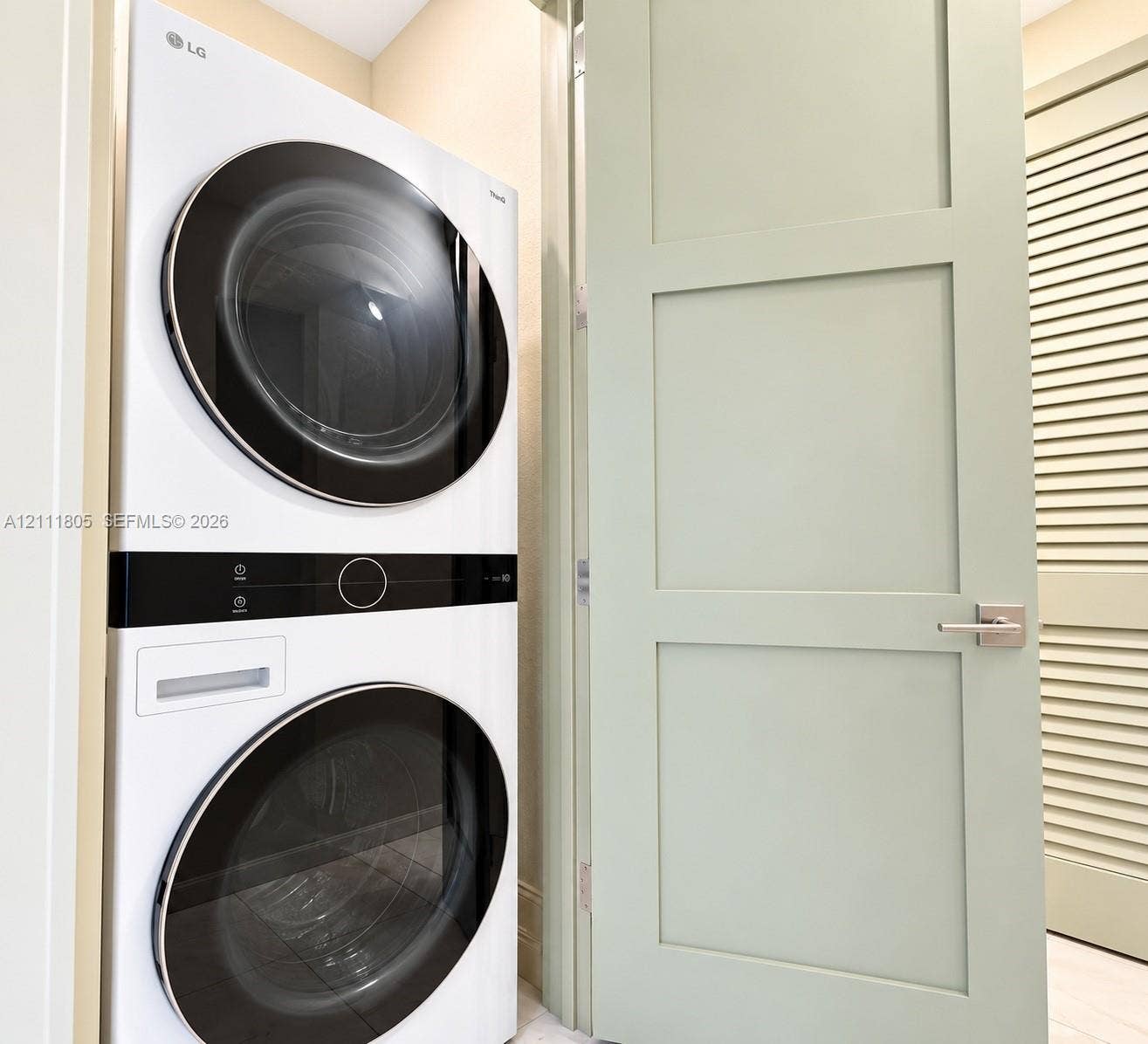 Stacked white LG washer and dryer unit with circular glass doors and central digital interface, pale green shaker-style door with satin nickel lever hardware, and louvered panel door