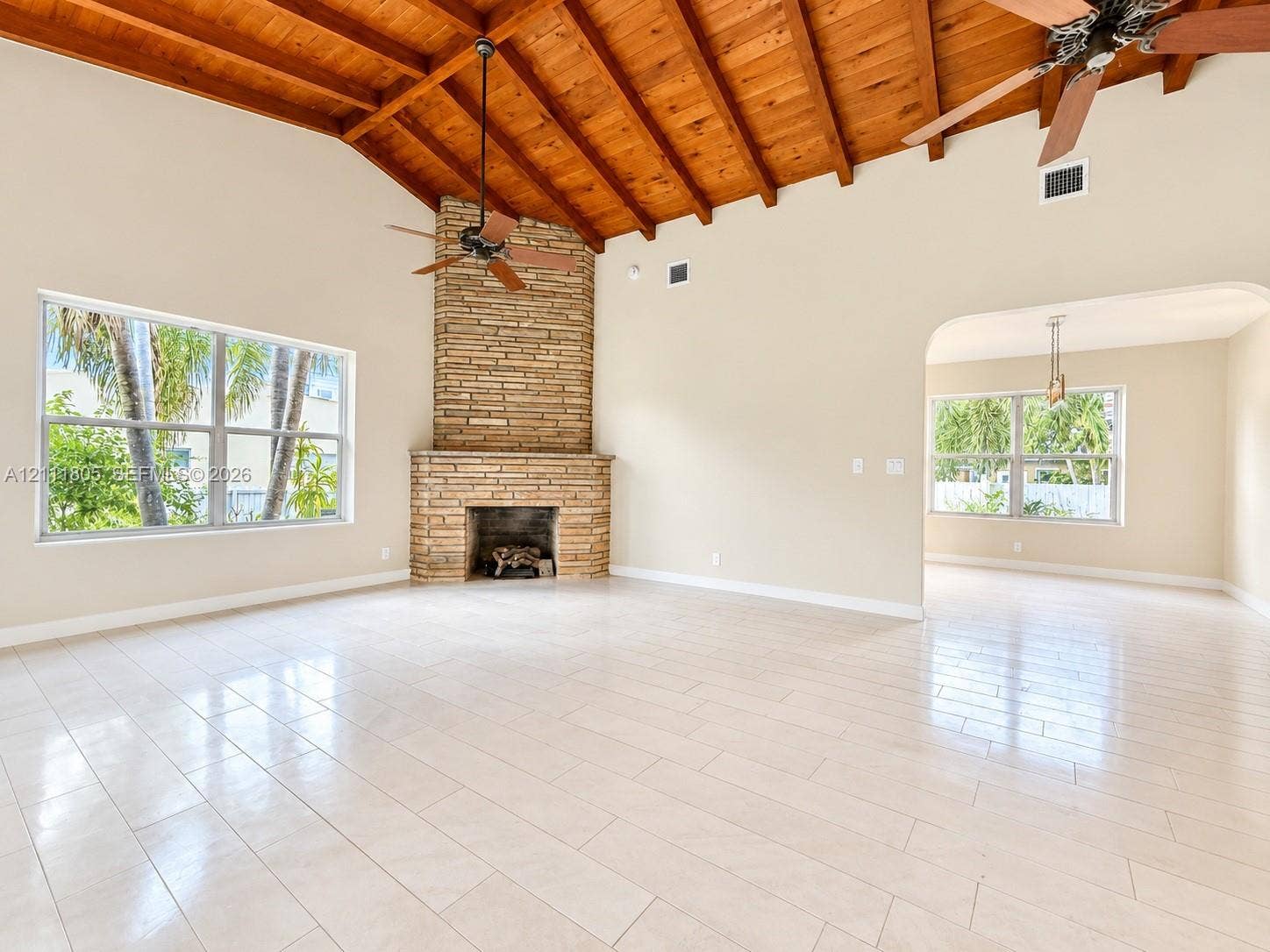 Vaulted wood-plank ceiling with exposed rafters, floor-to-ceiling stone masonry fireplace, and large-format tile flooring