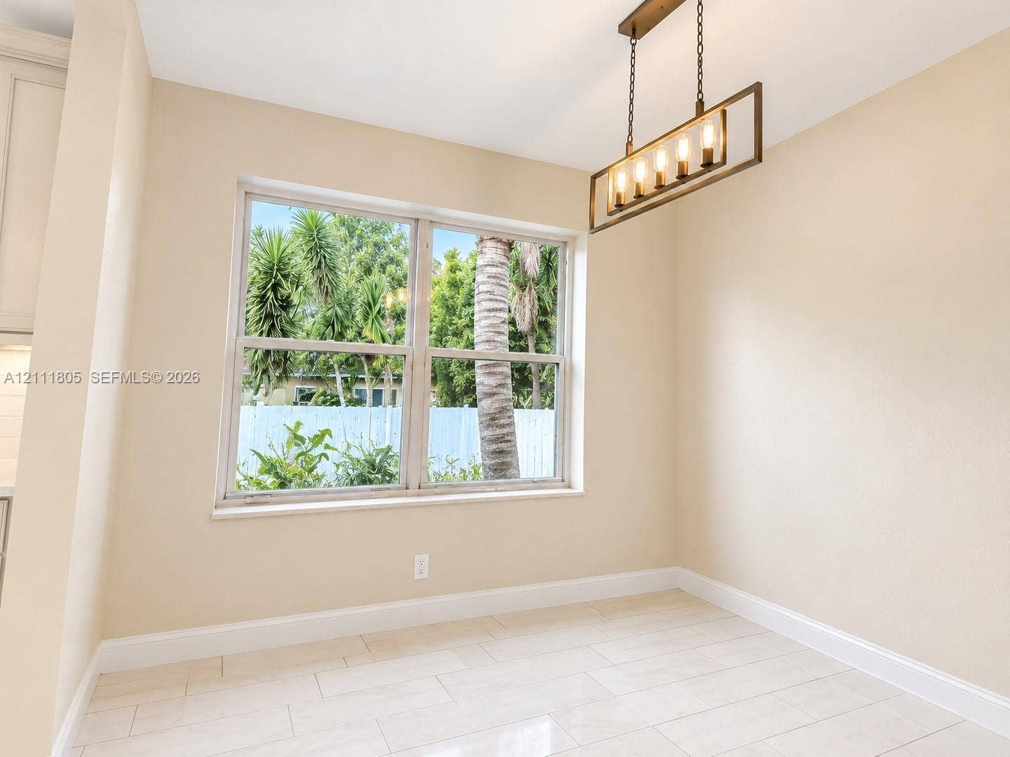 Neutral-toned interior space featuring light-colored tile flooring, large double-pane window, and a linear multi-bulb metal pendant light fixture