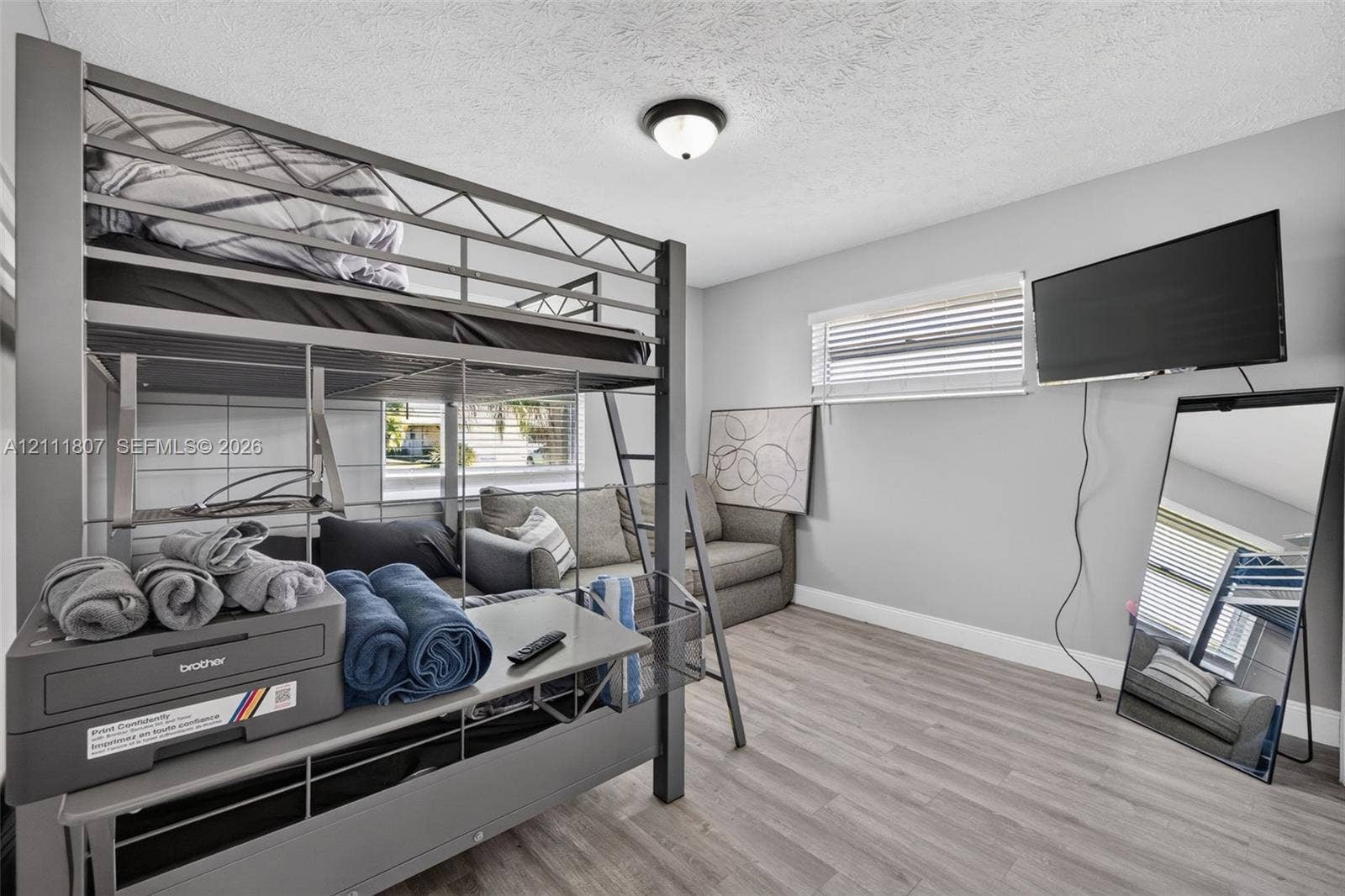 Room featuring light-toned wood-finish flooring, neutral wall paint, and horizontal window blinds with a flush-mount ceiling light fixture