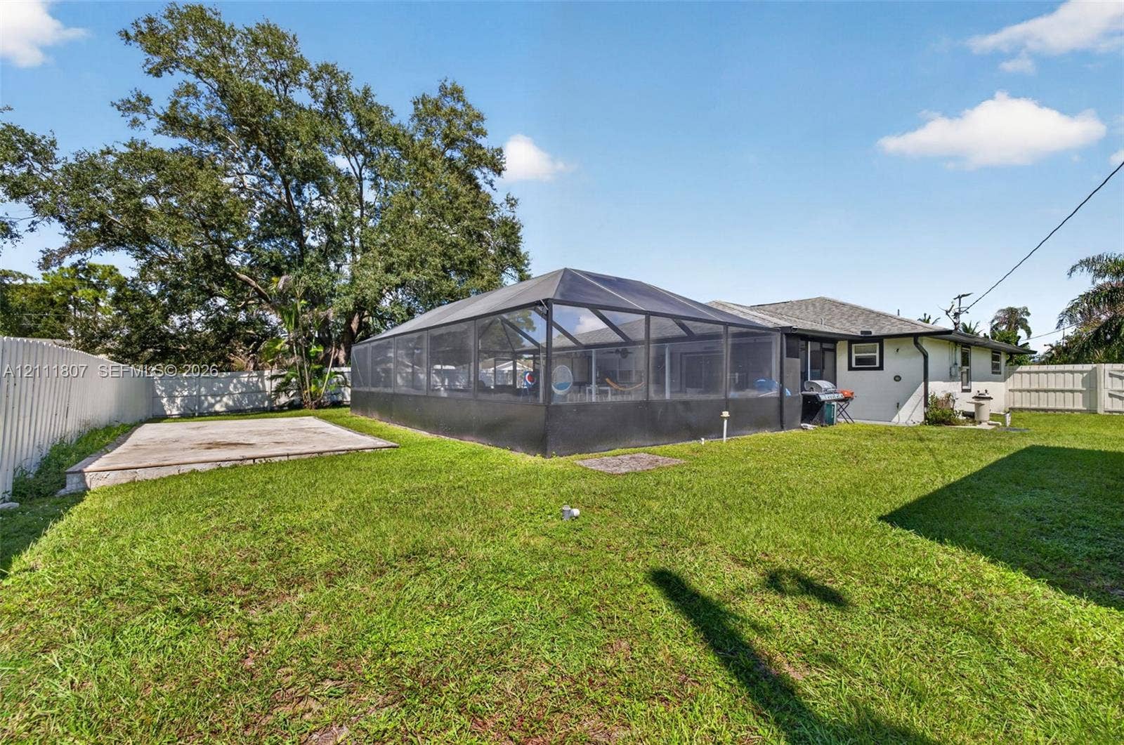 Backyard featuring a screened-in enclosure, concrete patio, white vinyl fencing, and mature trees