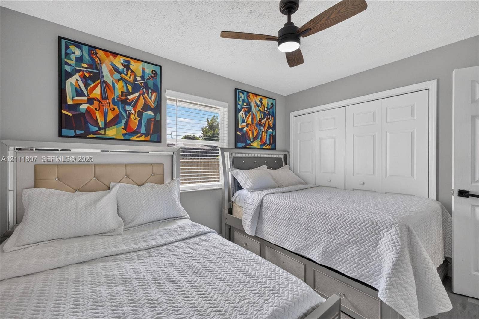 Neutral-toned bedroom featuring a matte black ceiling fan with integrated lighting, white dual-panel closet doors, horizontal blind window treatment, and gray interior walls