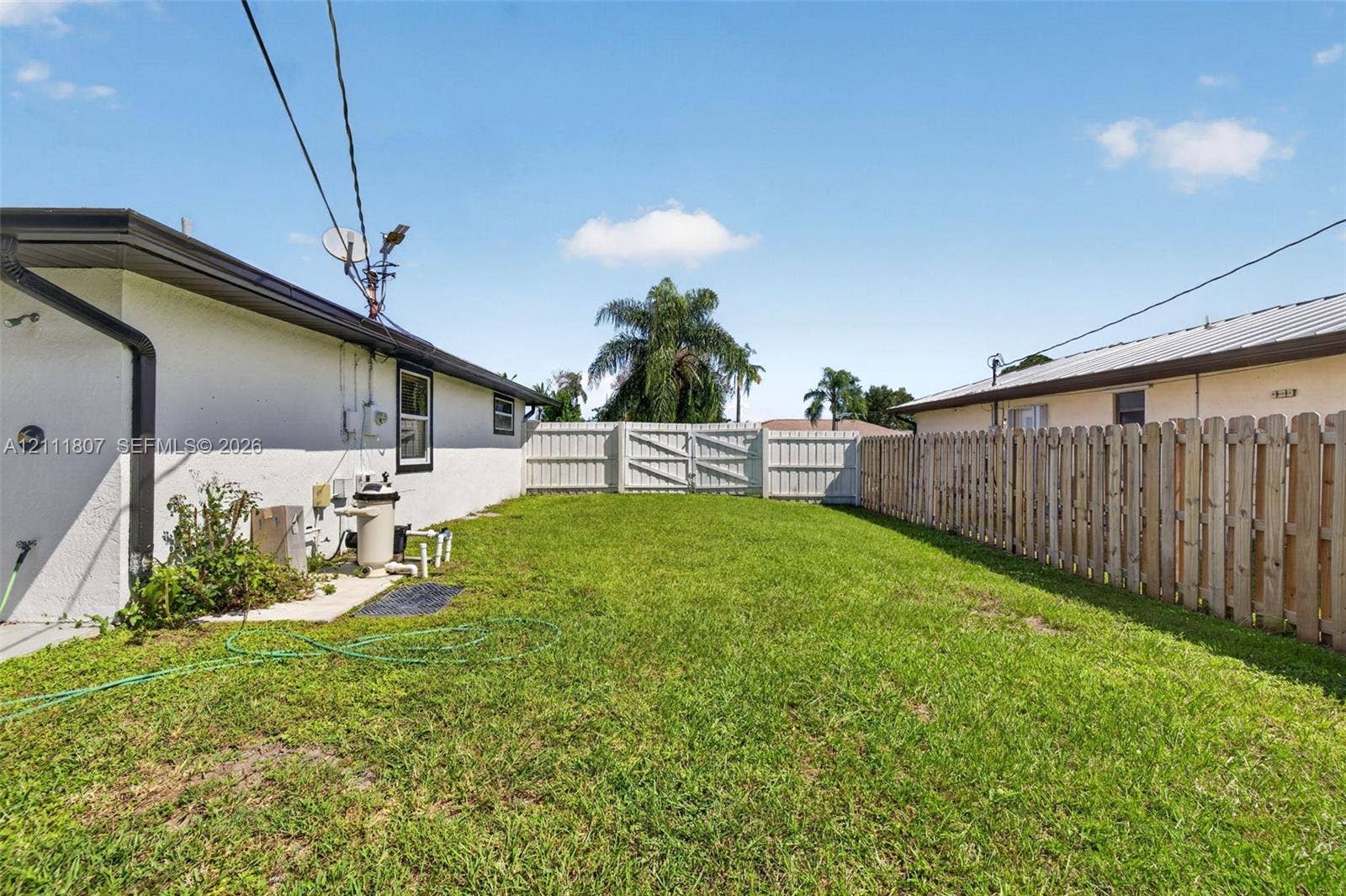 Backyard featuring a grass lawn, perimeter wood fencing, and a double-gate enclosure