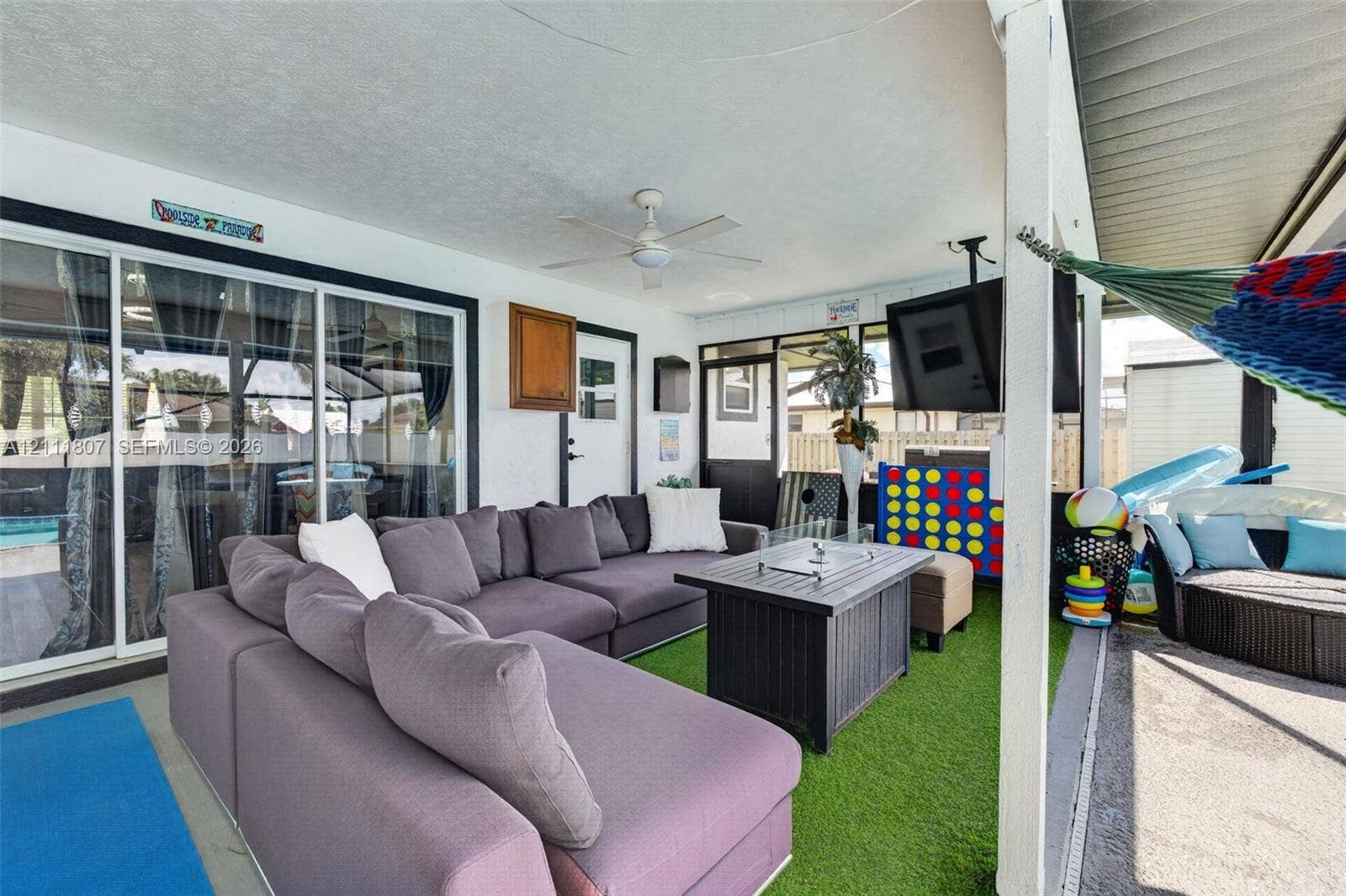 Covered patio featuring a ceiling fan, sliding glass doors, synthetic grass flooring, and screen enclosure