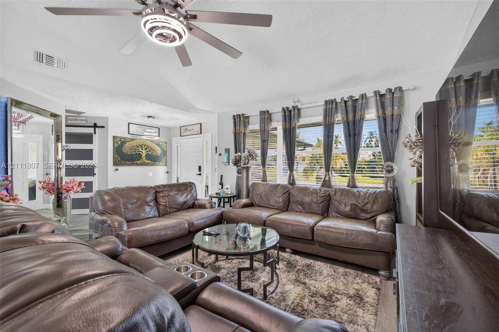 Vaulted ceilings featuring a central multi-light ceiling fan, large windows with horizontal blinds, and a sliding barn-style door