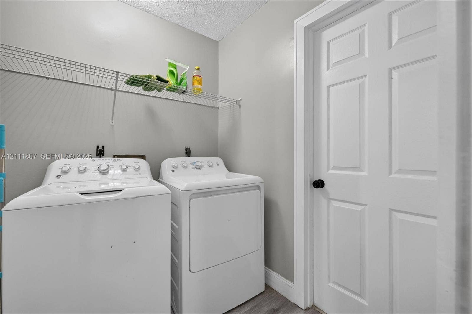Dedicated laundry area featuring a white six-panel door, wall-mounted wire shelving, and neutral-toned wall paint
