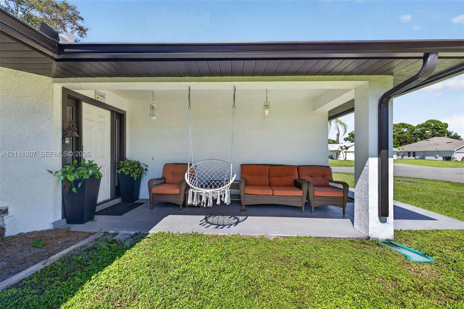 Covered front porch featuring smooth concrete flooring, dark trim, integrated ceiling lighting, and a paneled entry door