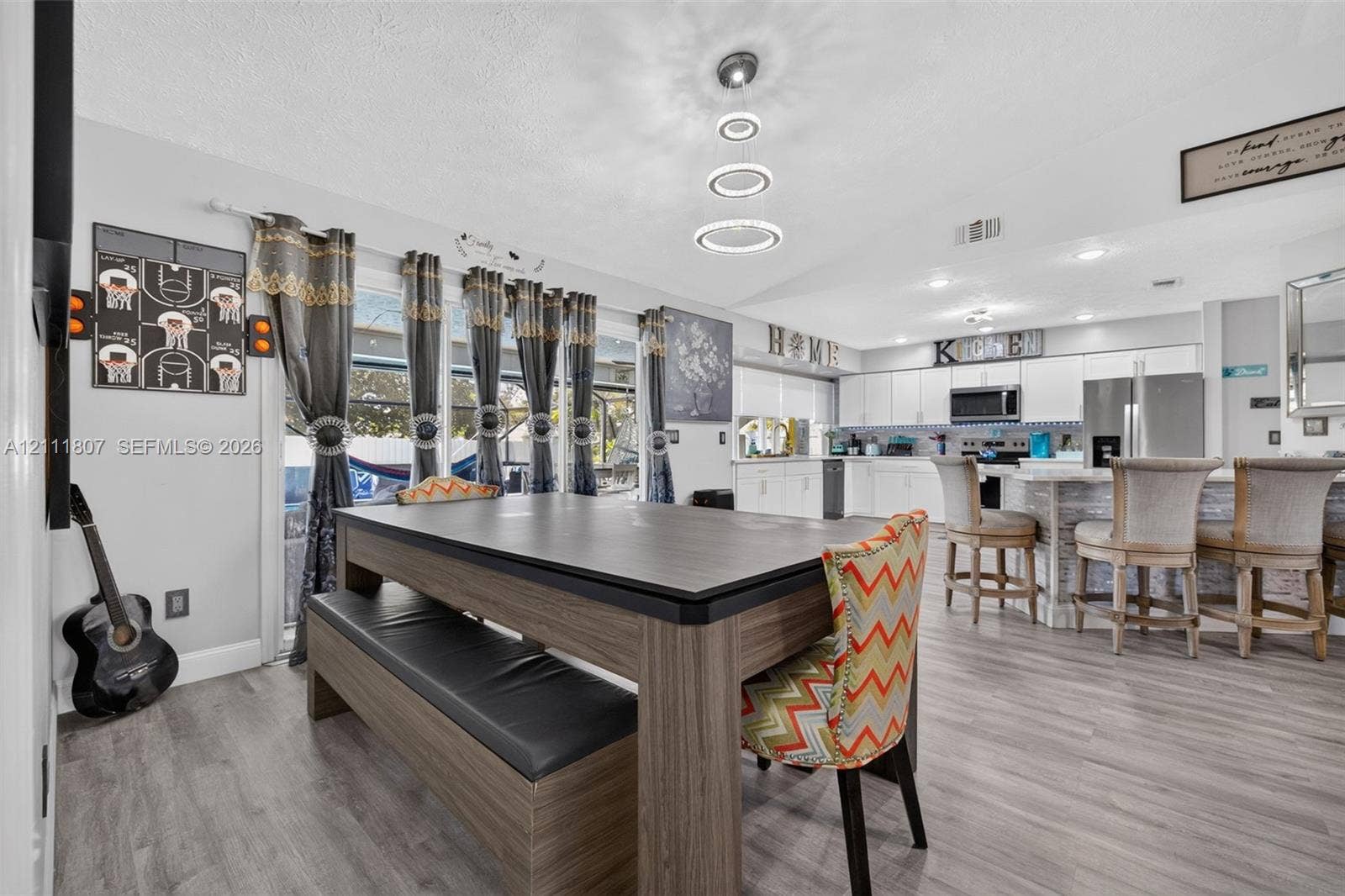 Open-concept interior featuring wood-finish flooring, a kitchen with white cabinetry, a breakfast bar, recessed lighting, and a modern multi-ring pendant light fixture