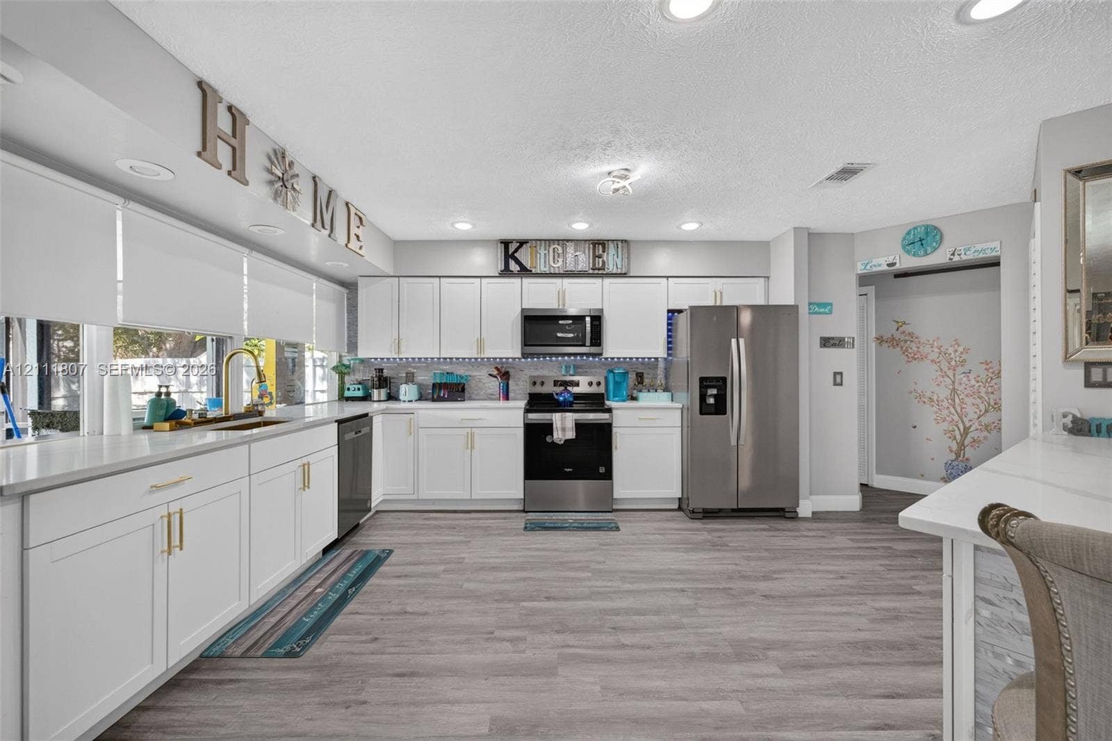 Kitchen featuring white shaker-style cabinetry, stainless steel appliances, wood-finish flooring, recessed lighting, and a neutral tile backsplash
