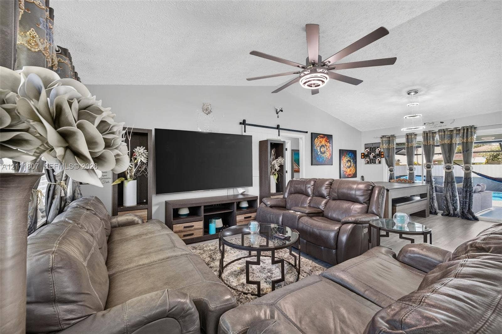 Vaulted ceilings featuring a multi-blade ceiling fan with integrated lighting, wood-finish flooring, built-in shelving, and a dark-finish sliding barn door