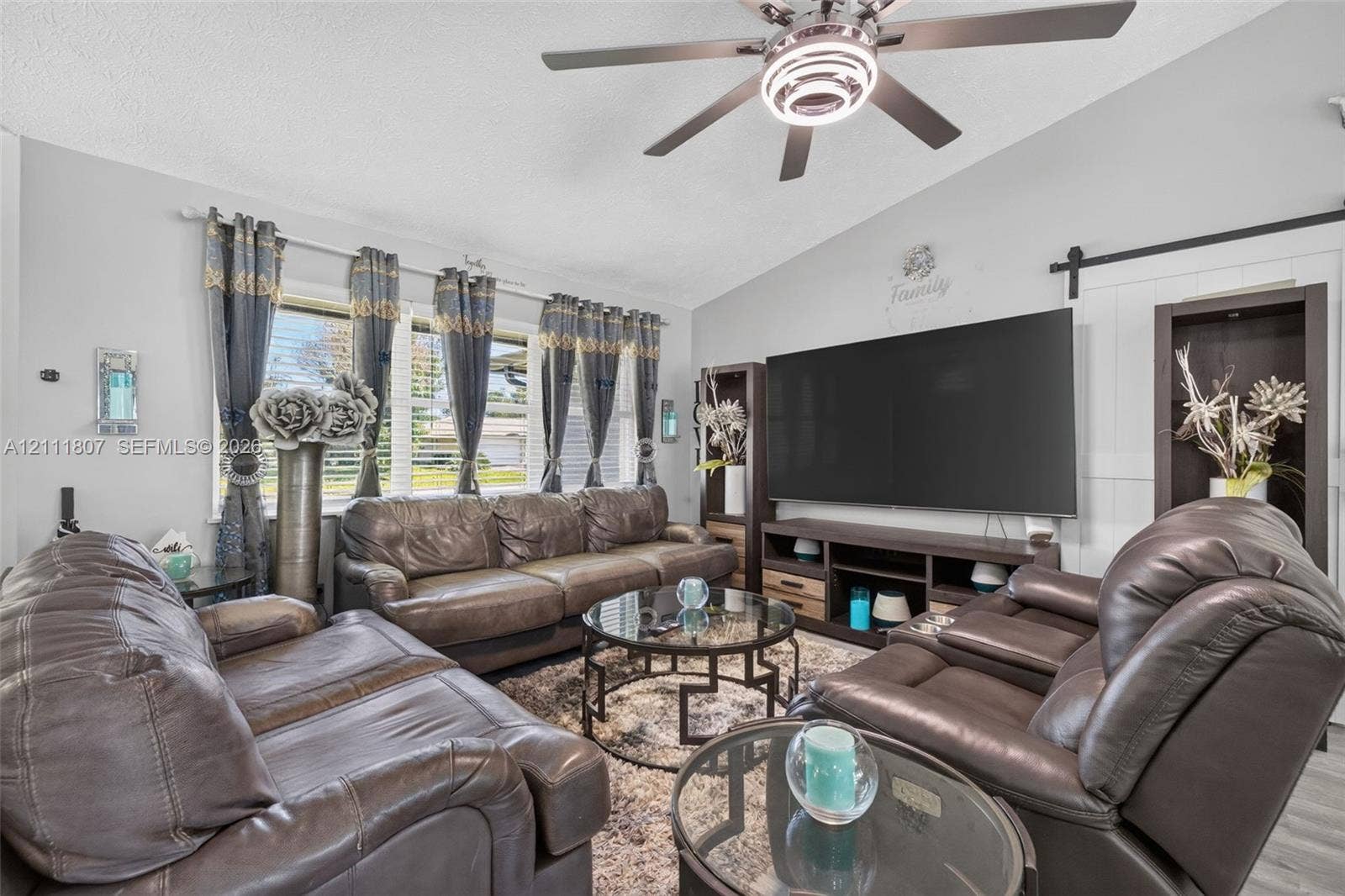 Vaulted ceiling featuring a central multi-blade ceiling fan with integrated lighting, oversized window configuration, and white sliding barn door