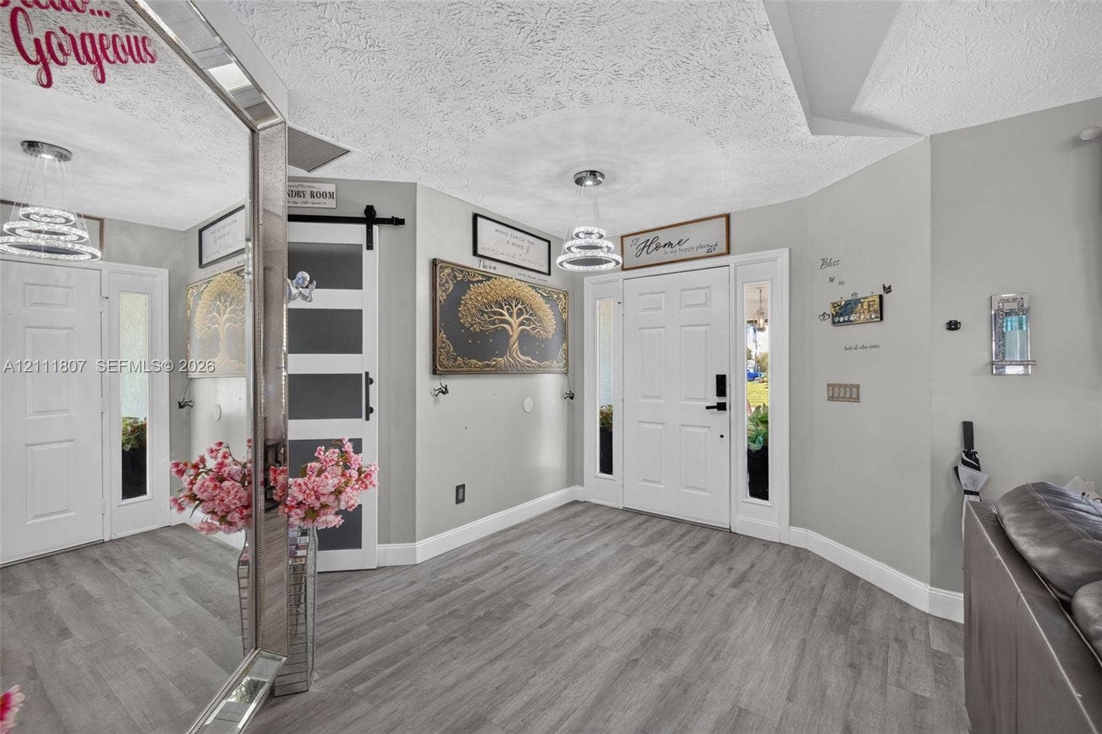 Entryway featuring wood-finish flooring, a sliding barn door with glass panes, white six-panel doors with side lites, and multi-tiered modern pendant lighting