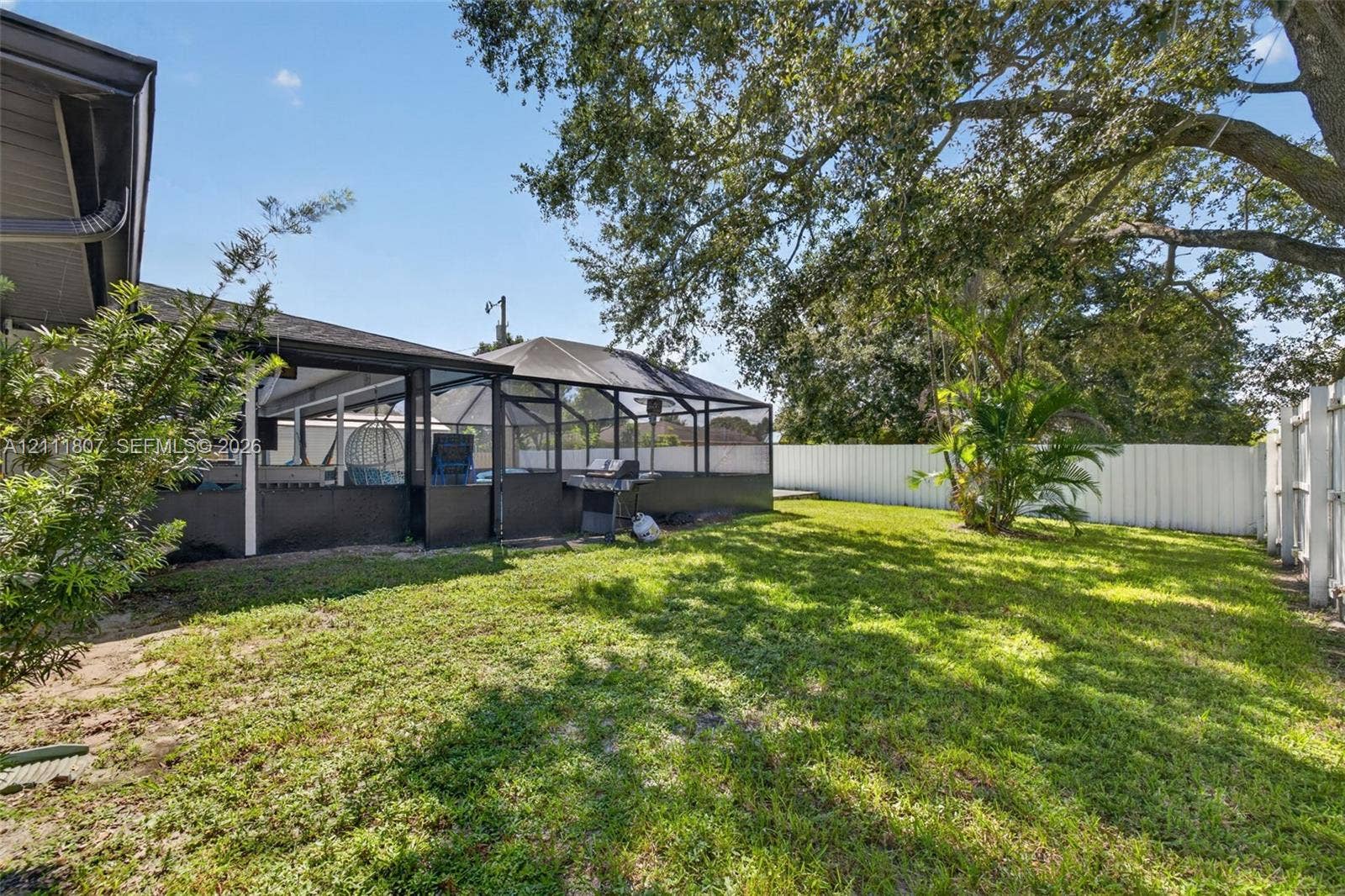Backyard featuring a screened-in lanai, privacy fencing, mature trees, and a grass lawn