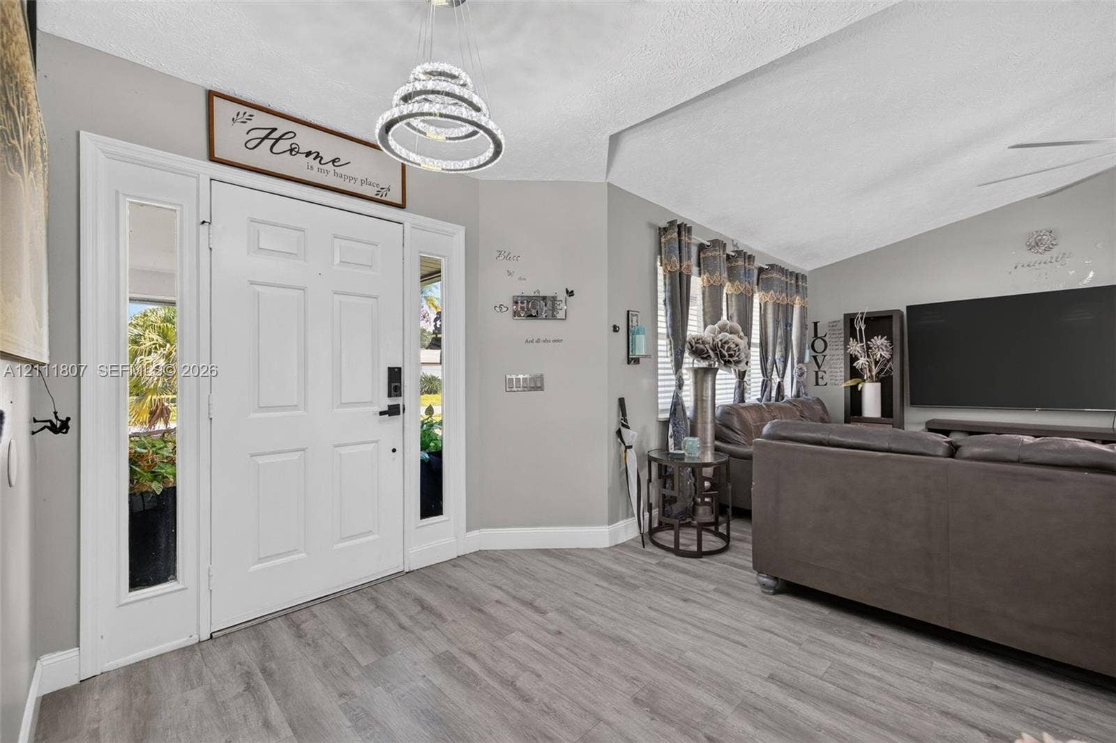 Entryway featuring a multi-paneled white door with dual sidelights, wood-finish flooring, vaulted ceiling, and a tiered crystal-style chandelier