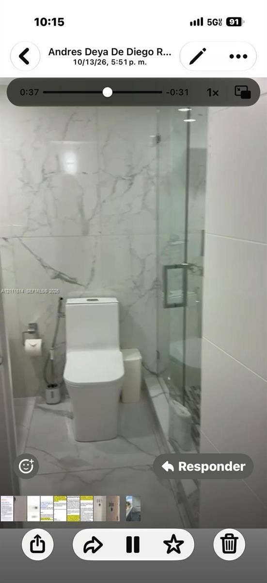 Bathroom featuring large-format veined porcelain tile wall and floor surfaces, glass-enclosed shower, and a minimalist low-profile dual-flush toilet