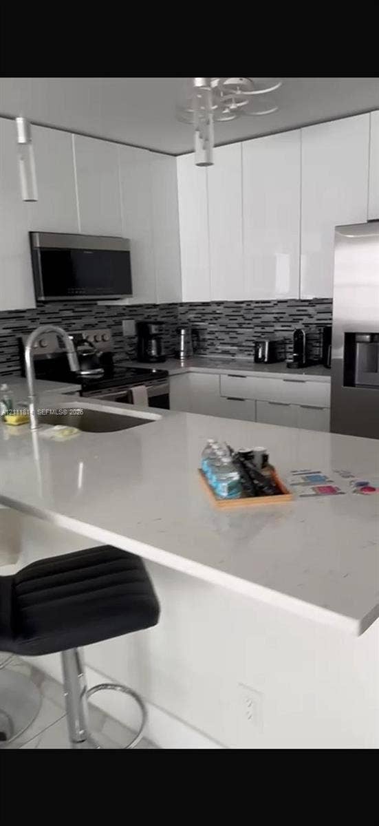 Kitchen featuring gloss-finish cabinetry, stone-surface countertops, stainless steel appliances, a multi-tone tile backsplash, and a built-in island