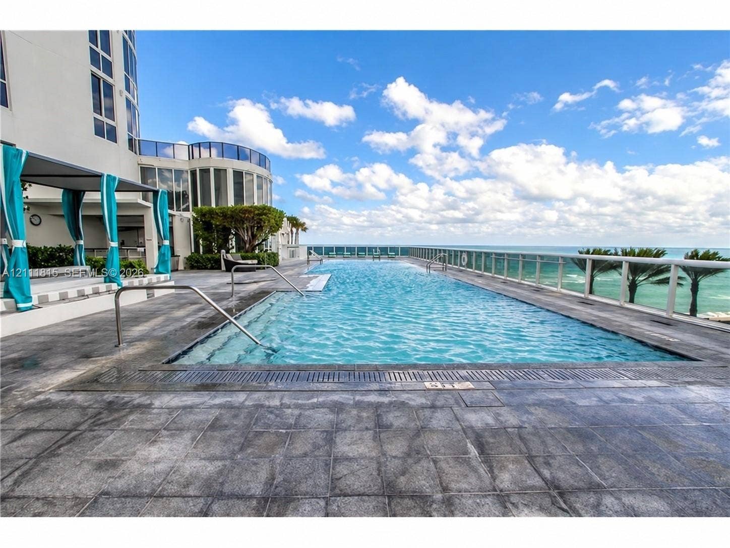 15811 Collins Avenue, #4102, Sunny Isles Beach, FL 33160 Infinity-edge swimming pool with metal handrails and stone tile decking, featuring a glass panel perimeter railing and oceanfront orientation