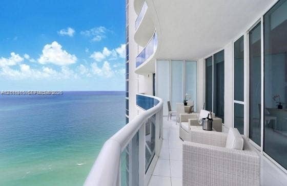 15811 Collins Avenue, #4102, Sunny Isles Beach, FL 33160 Expansive curved balcony featuring floor-to-ceiling glass railings, large-format tile flooring, and full-height glass sliding door access