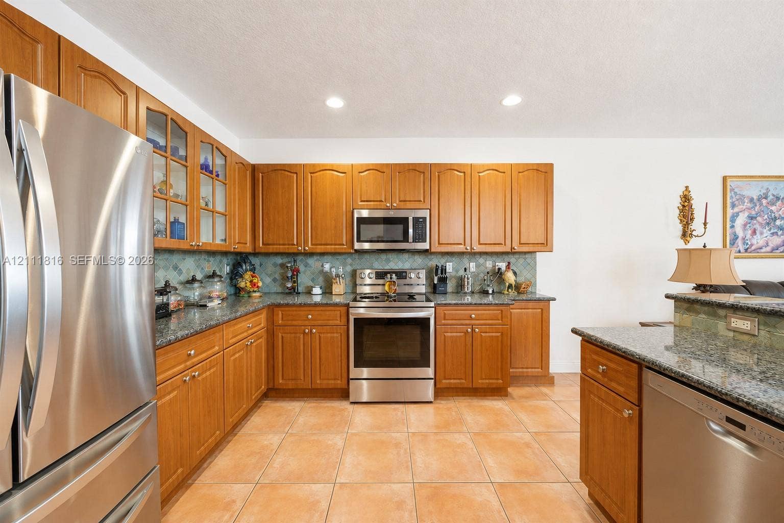 Kitchen featuring stained wood cabinetry, stone countertops, stainless steel appliances, a decorative tile backsplash, and tile flooring