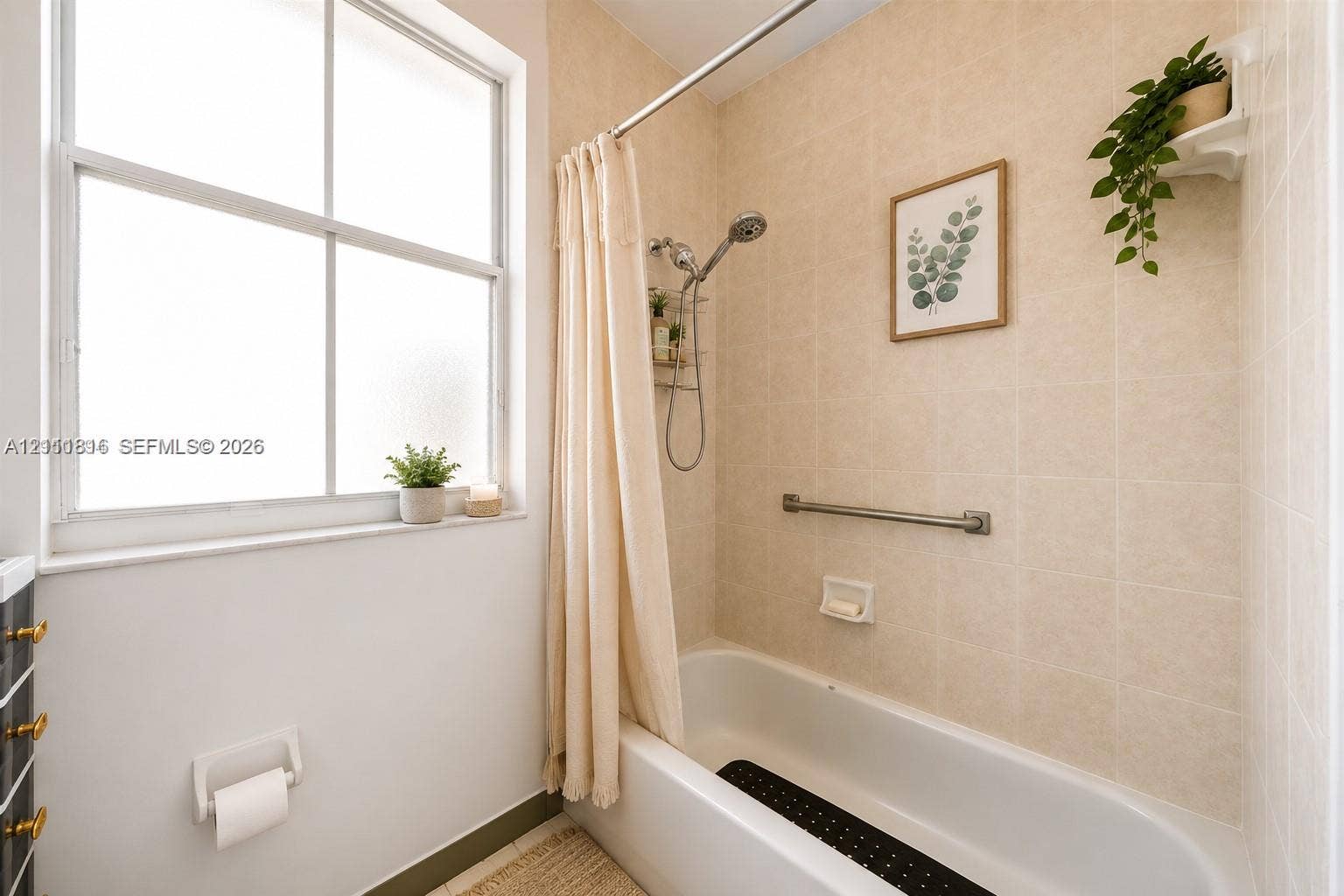 Full bathroom featuring a white porcelain tub, wall-mounted brushed metal grab bar, adjustable shower head, and neutral tiled surround