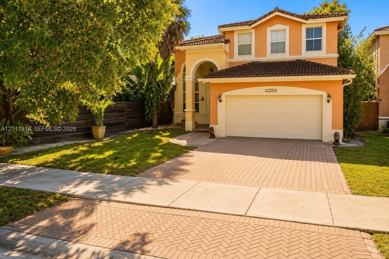 Two-story exterior featuring a stucco faade, tiled roof, arched entryway, and a herringbone-patterned paved driveway