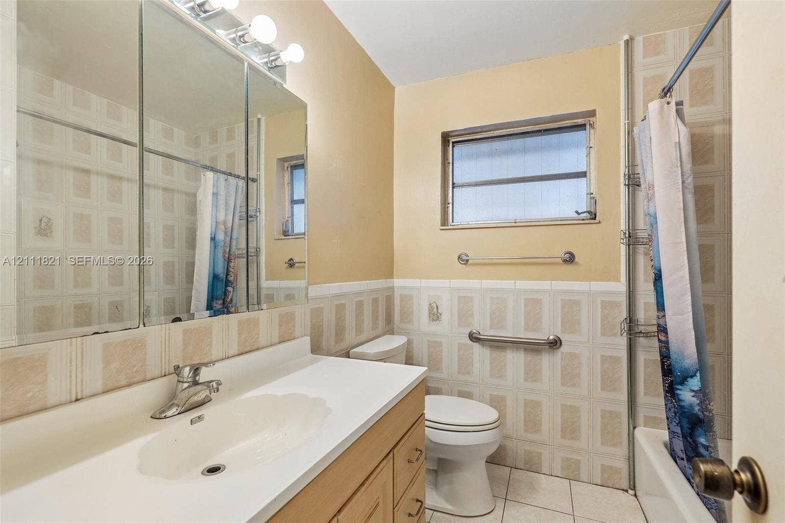 Bathroom featuring a vanity with an integrated sink and countertop, a multi-panel mirrored medicine cabinet, a tiled tub surround, and installed wall-mounted grab bars