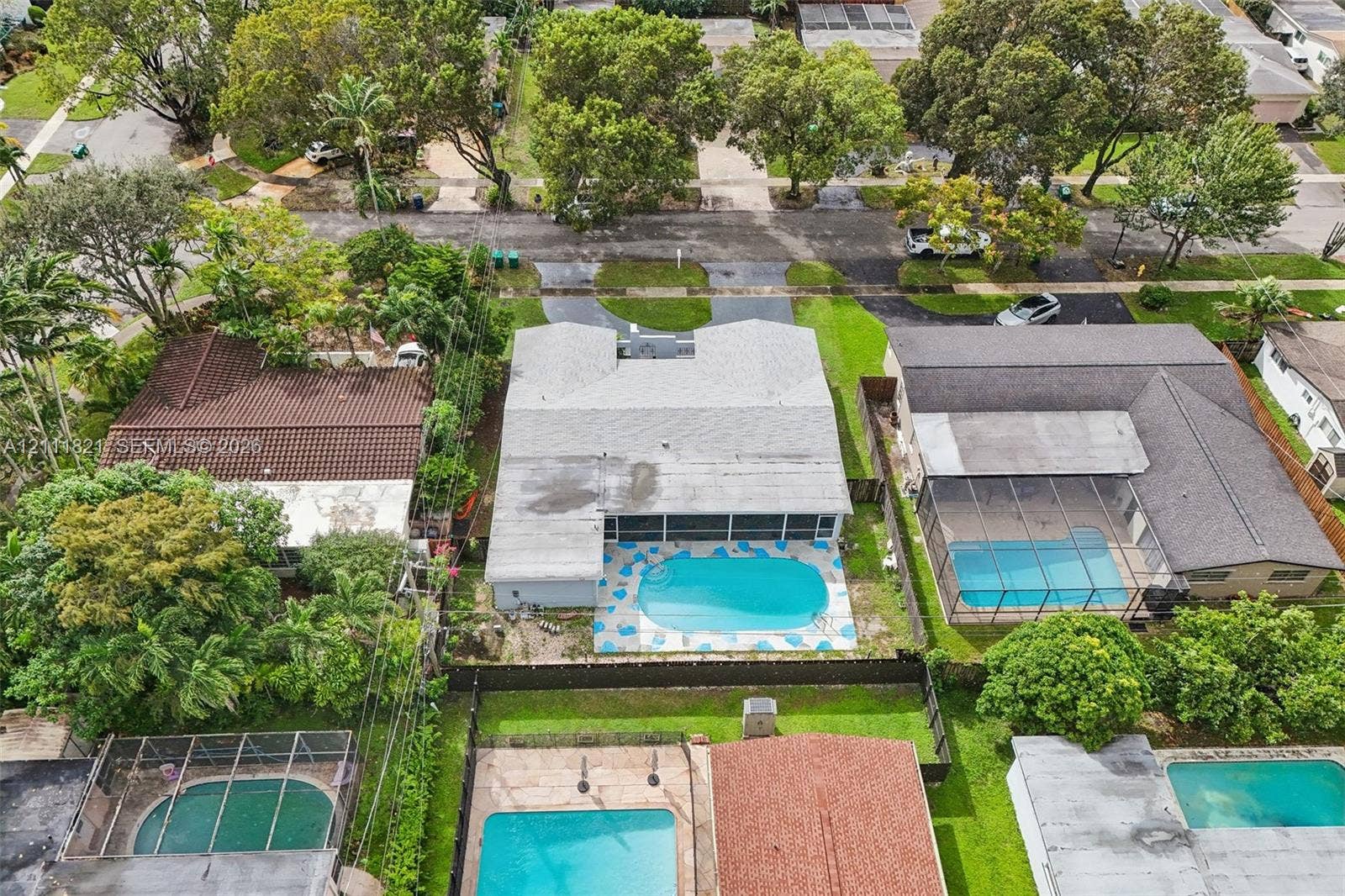 Aerial perspective of a property featuring an in-ground swimming pool, a screened-in patio, and mature landscaping