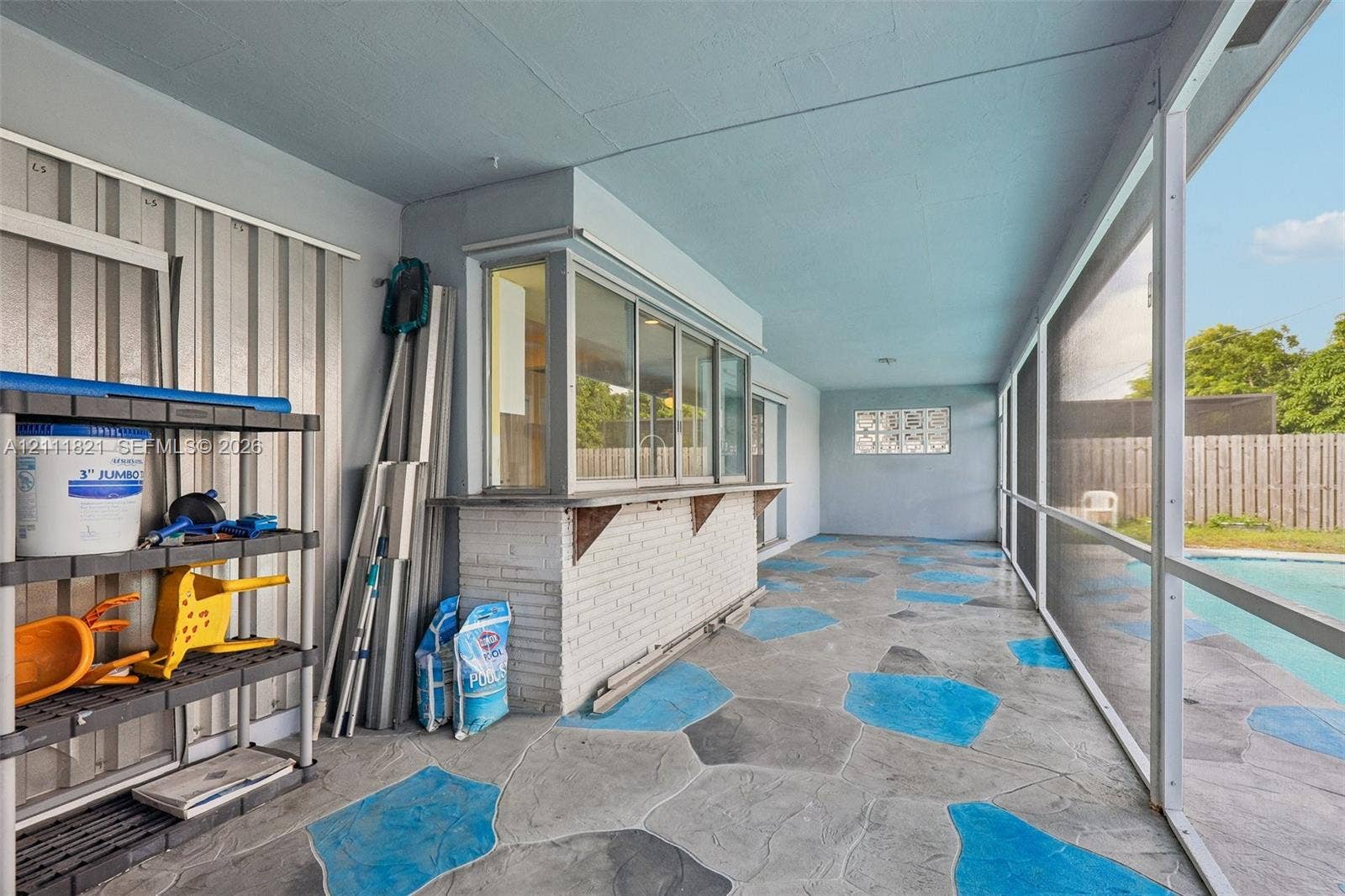 Screened-in lanai featuring decorative stone-patterned concrete flooring, a white brick service bar with a pass-through window, and a privacy-fenced exterior