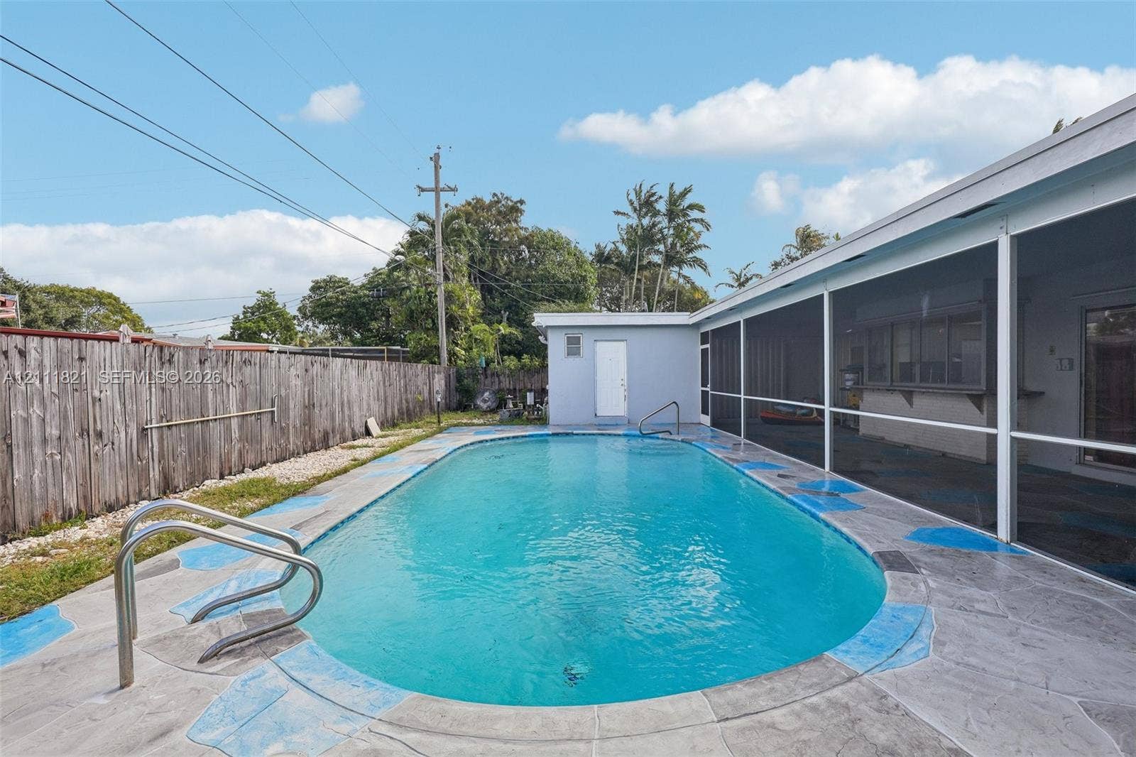 In-ground swimming pool with a metal handrail, surrounded by a concrete pool deck and an attached screen enclosure