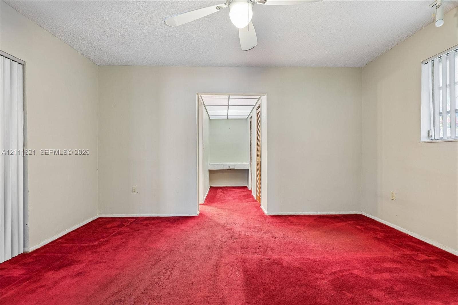 Room featuring wall-to-wall carpeting, ceiling-mounted light fixture with fan, and a pass-through opening to a vanity area with built-in cabinetry