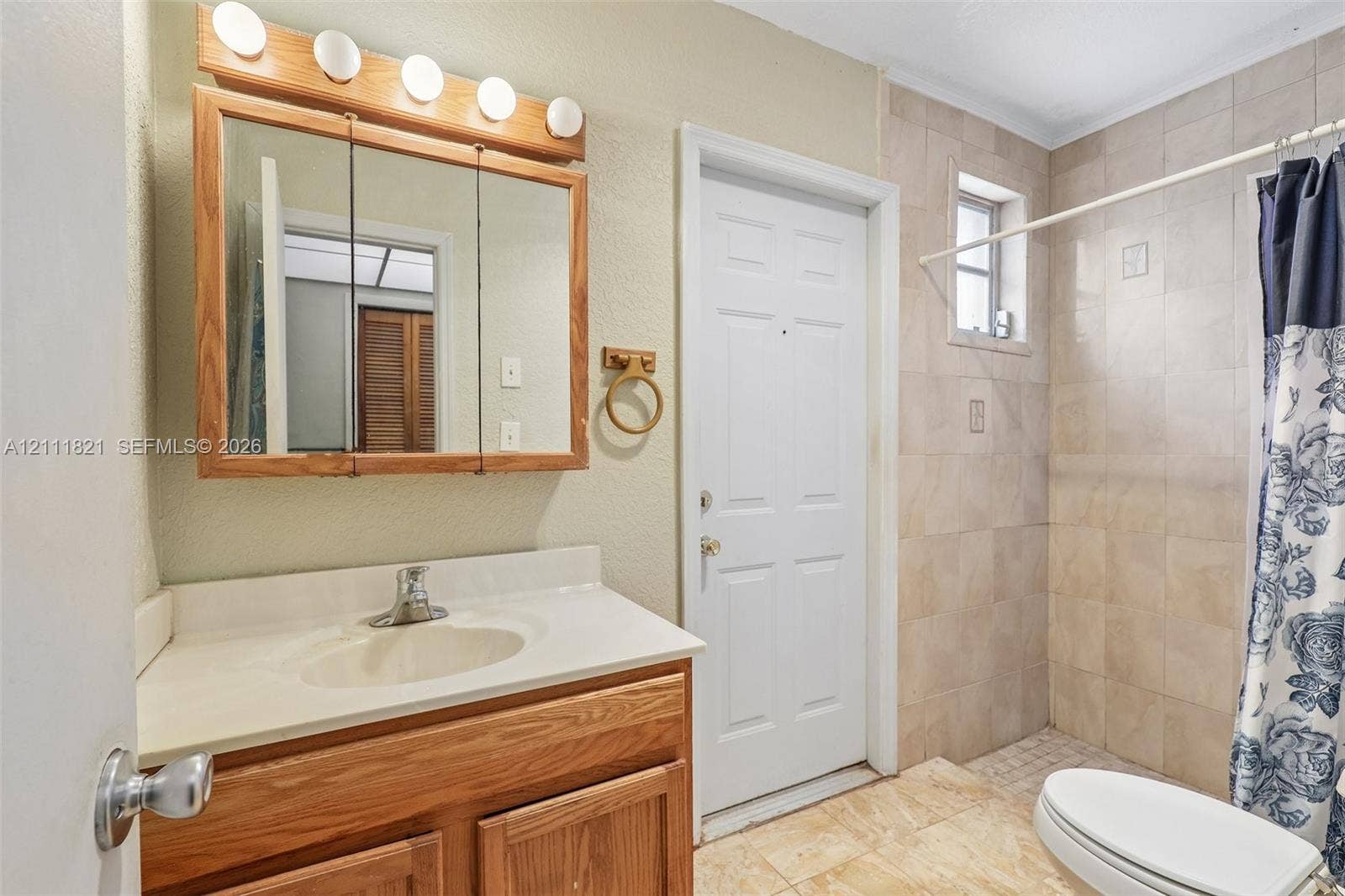 Bathroom featuring a wood-tone vanity cabinet with an integrated countertop, a tri-fold mirrored medicine cabinet with integrated lighting, and tile-surround shower walls