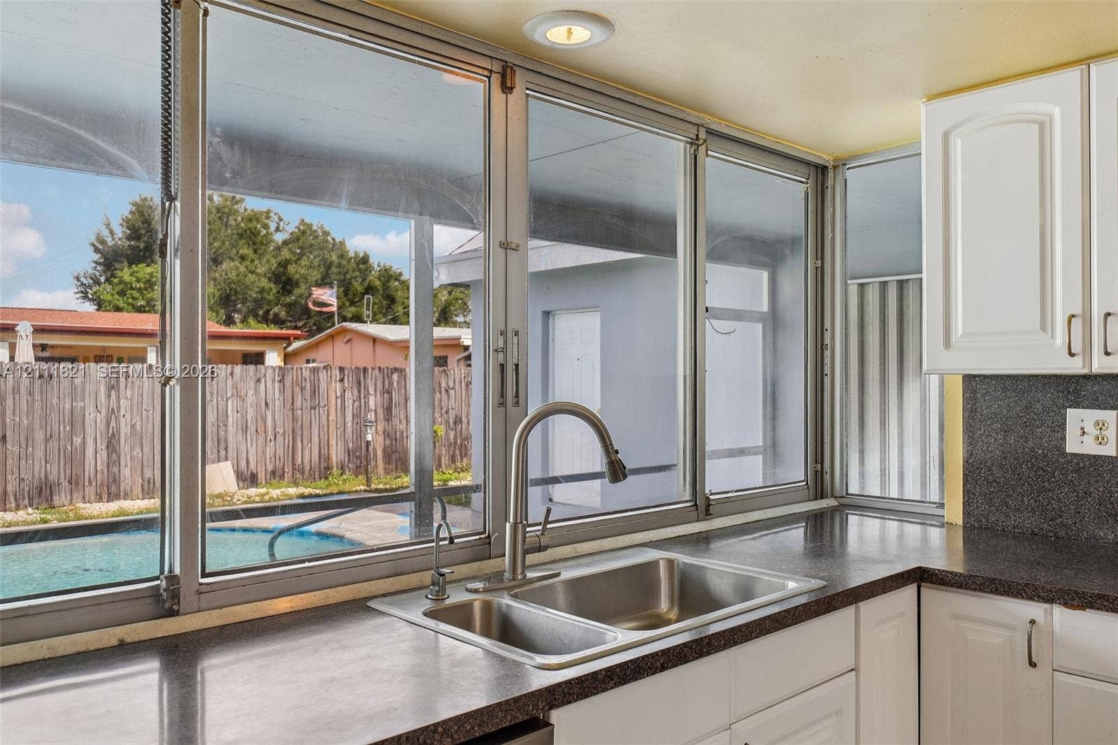 Kitchen sink featuring a dual-basin stainless steel basin, high-arc faucet, solid-surface countertops, white cabinetry, and multi-pane window configuration