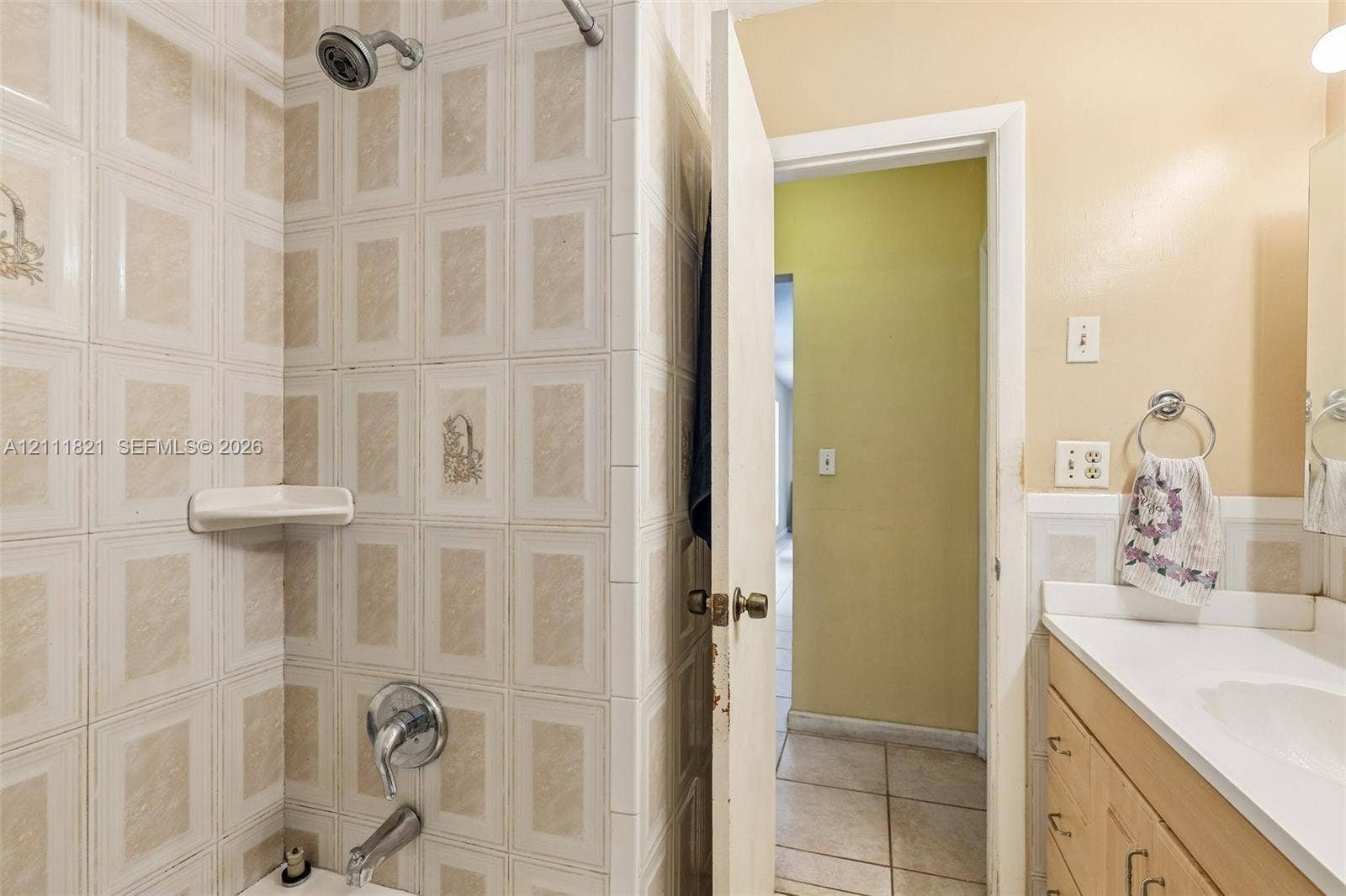 Bathroom featuring a tiled shower enclosure with integrated shelving, chrome shower fixtures, white vanity cabinet with countertop, and ceramic floor tile