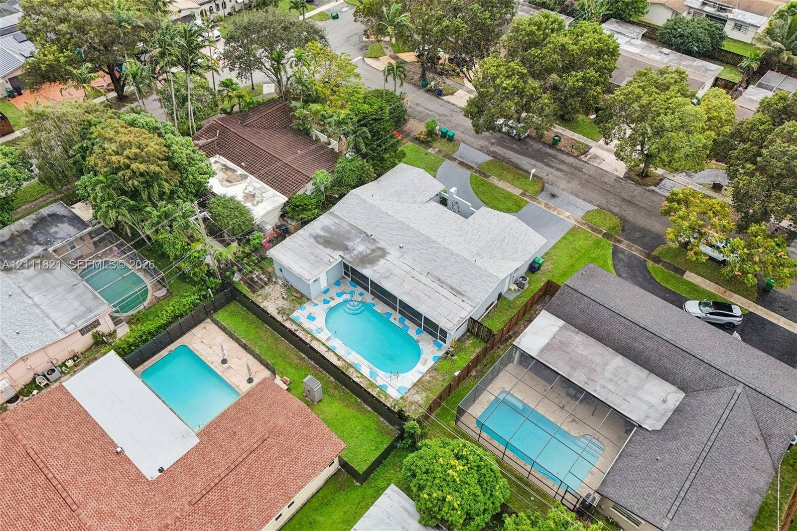 Aerial perspective featuring a shingled roof, an in-ground swimming pool, a screened-in lanai, and a fenced-in grass backyard