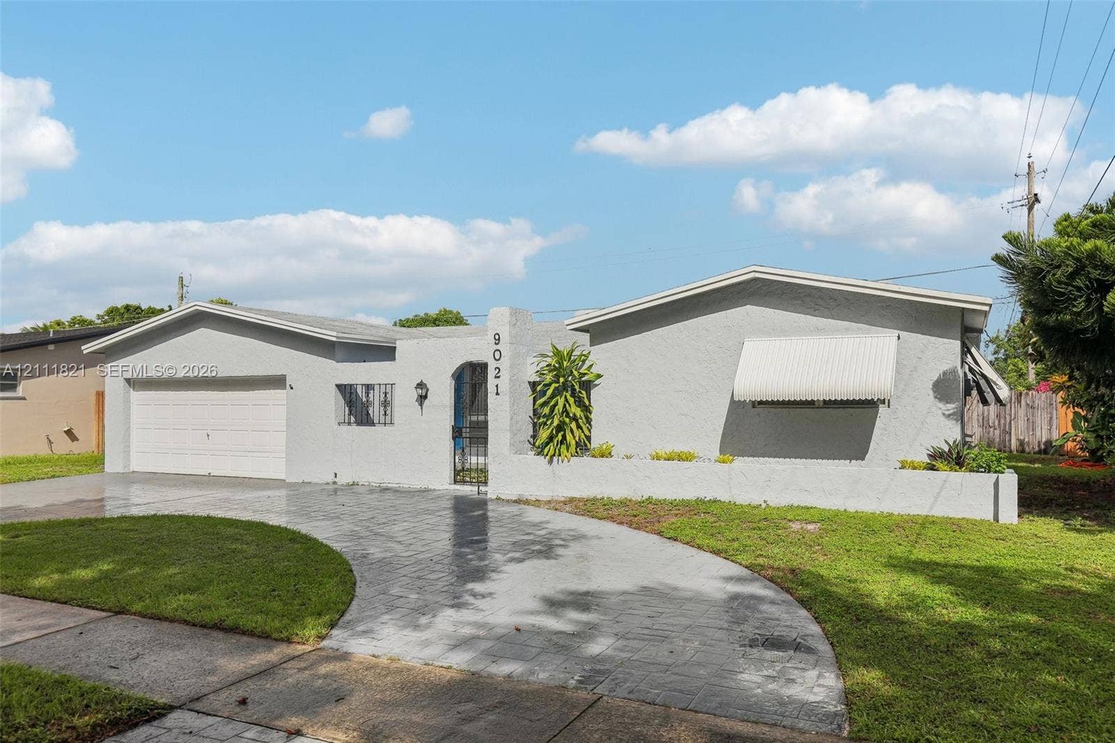 Single-story residence featuring a gray stucco exterior, arched entry, stamped concrete driveway, attached garage, and fixed window awnings