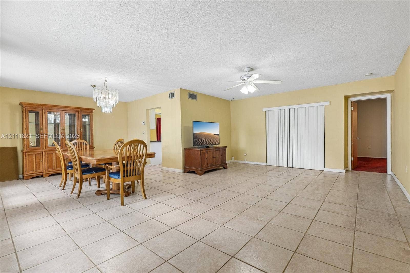 Open-concept interior featuring light-colored ceramic tile flooring, a multi-light crystal-style chandelier, a ceiling fan with integrated lighting, and white sliding glass door panels