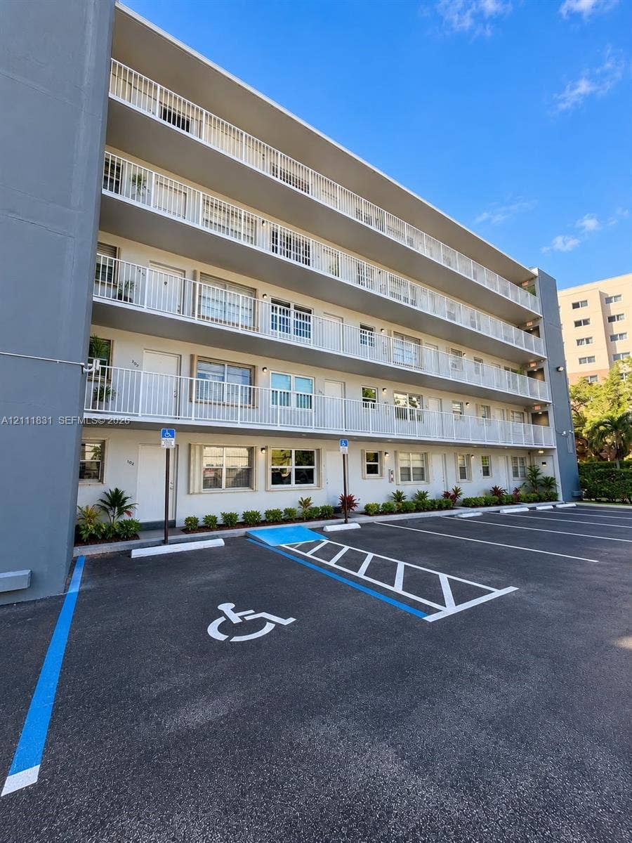 1629 N River Drive, #103, Miami, FL 33125 Multi-story exterior featuring white railed balconies, paved surface parking, and ground-level landscaping