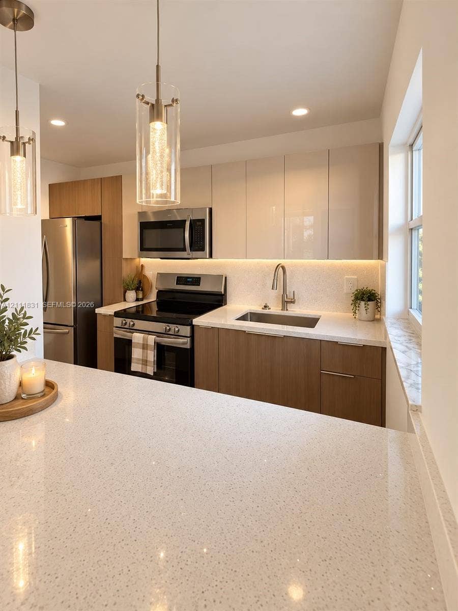 1629 N River Drive, #103, Miami, FL 33125 Kitchen featuring two-tone cabinetry with flat-panel doors, expansive stone-finish countertops, stainless steel appliances, under-cabinet lighting, and cylindrical pendant fixtures
