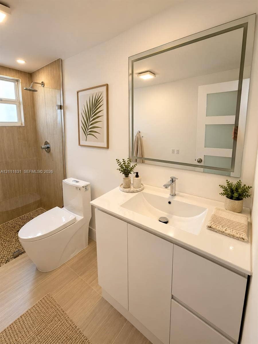 1629 N River Drive, #103, Miami, FL 33125 White vanity cabinet with an integrated sink and light-toned countertop, framed mirror, walk-in shower with tile surround, and neutral floor tiling