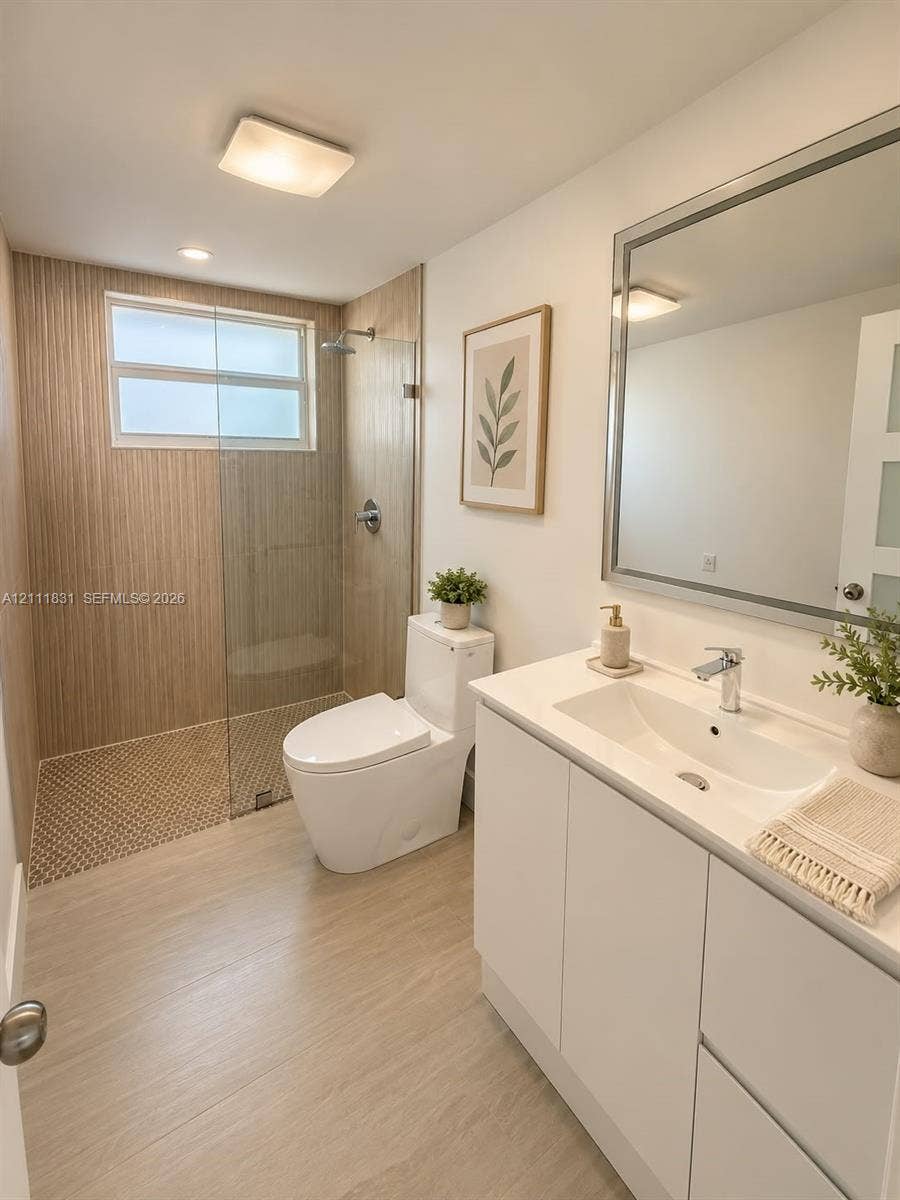 1629 N River Drive, #103, Miami, FL 33125 Bathroom featuring a walk-in shower with vertical tile surround and a glass partition, vanity with a white countertop and integrated sink, dual-flush toilet, and a framed mirror