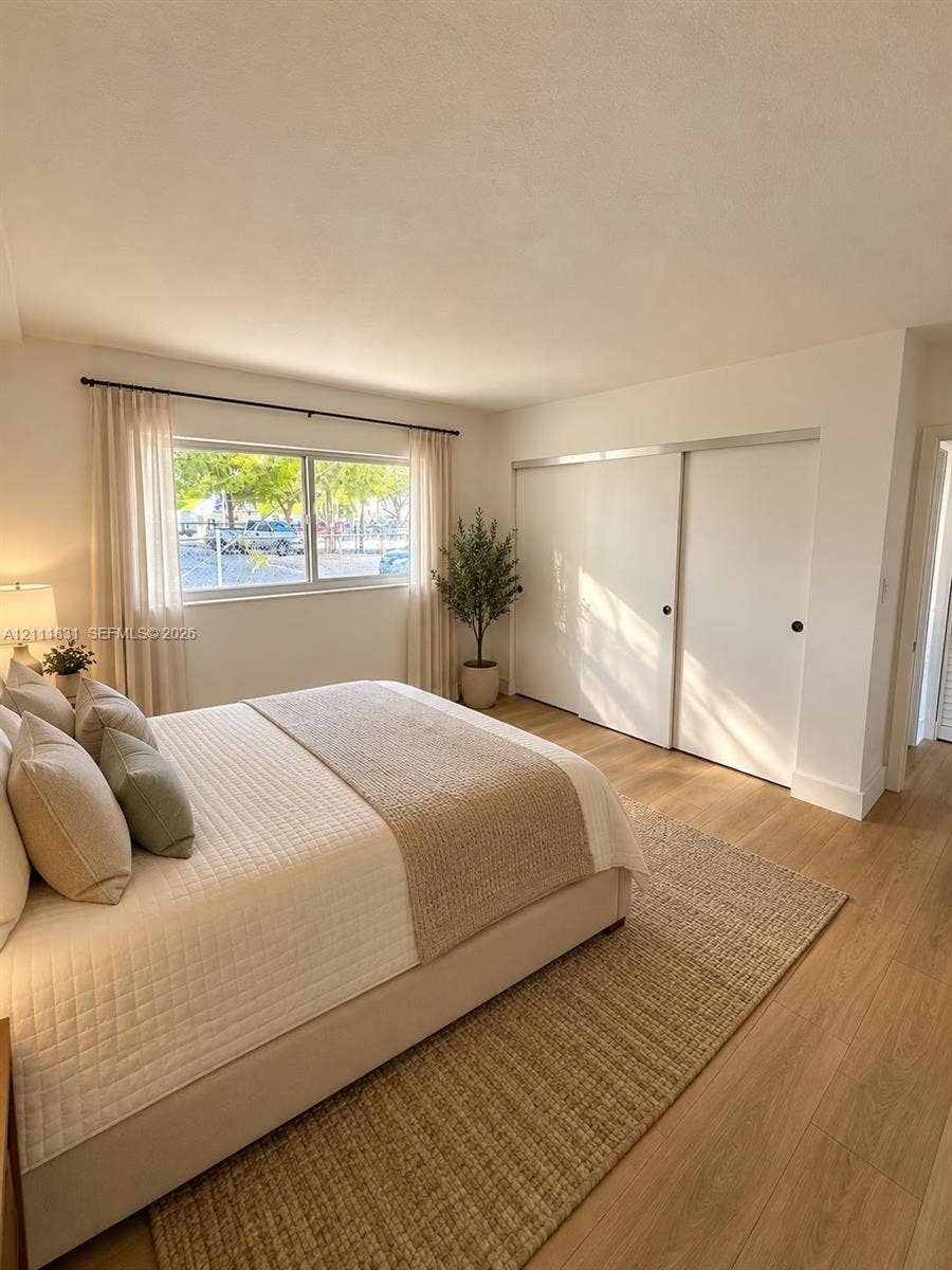 1629 N River Drive, #103, Miami, FL 33125 Neutral interior space featuring wood-finish flooring, a large horizontal window with a black metal rod, and built-in sliding closet doors