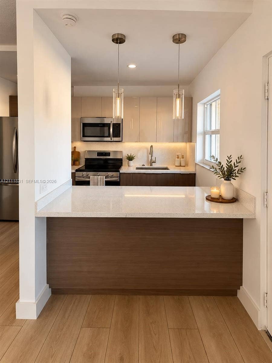 1629 N River Drive, #103, Miami, FL 33125 Kitchen featuring quartz countertops, two-tone cabinetry, stainless steel appliances, wood-finish flooring, and dual glass pendant lights