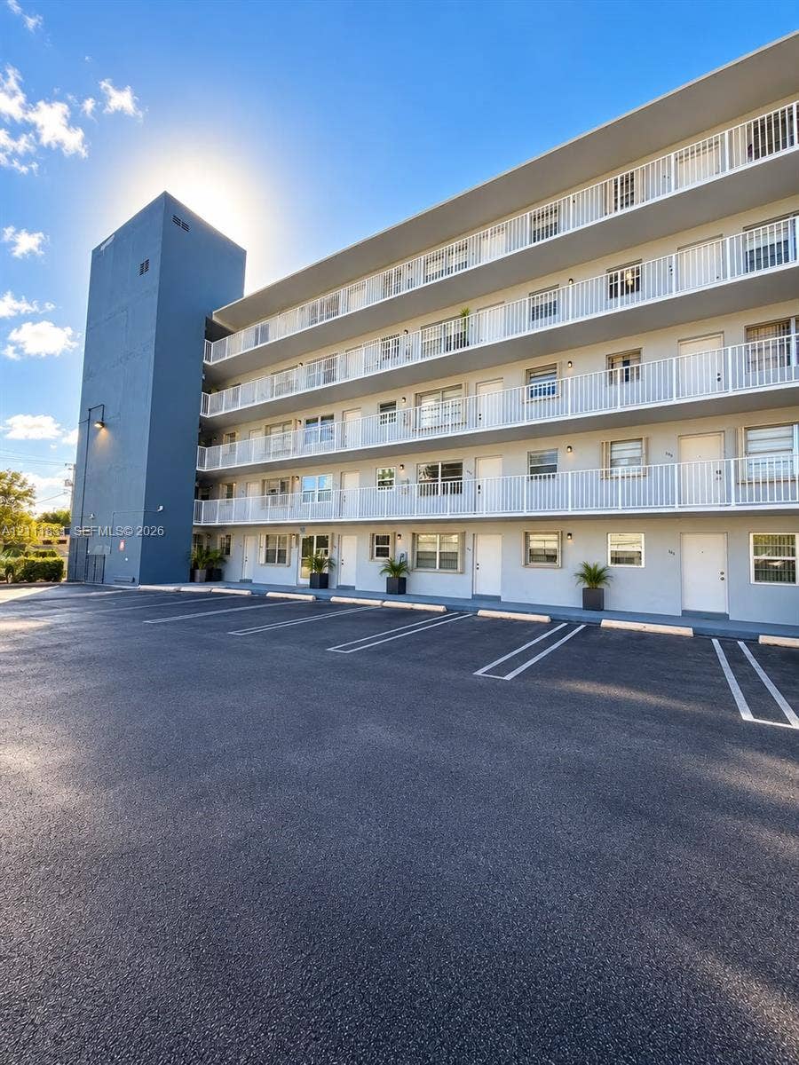 1629 N River Drive, #103, Miami, FL 33125 Multi-story exterior featuring a smooth stucco finish, asphalt-paved parking area, white metal balcony railings, and individual unit entry doors