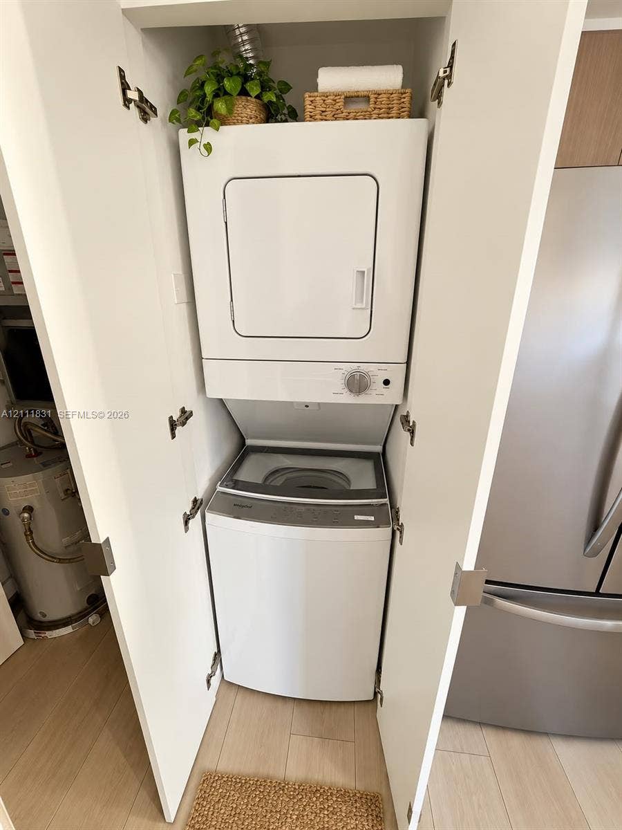 1629 N River Drive, #103, Miami, FL 33125 Stacked laundry unit housed within a dedicated closet featuring white cabinetry and light-toned flooring