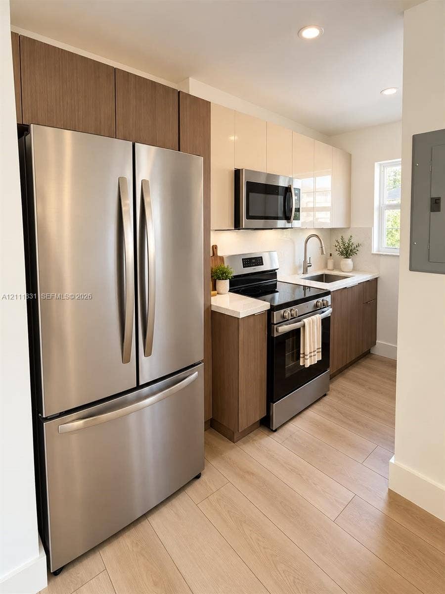 1629 N River Drive, #103, Miami, FL 33125 Kitchen featuring two-tone cabinetry with wood-finish lower units and high-gloss upper cabinets, stainless steel appliances, stone-surface countertops, and wood-finish flooring