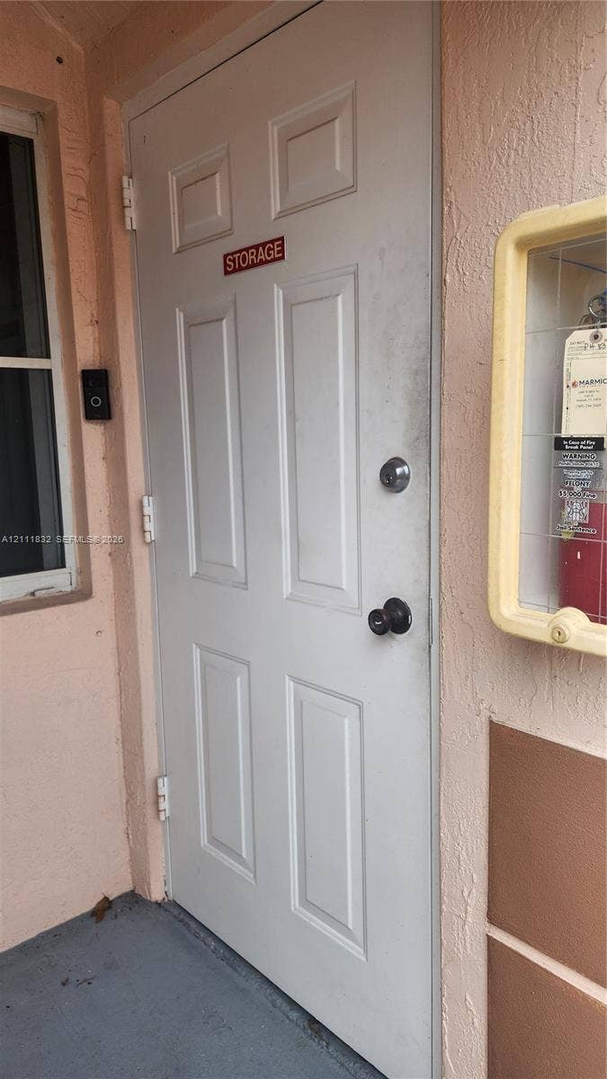 1250 SE 28th Court, #102, Homestead, FL 33035 Six-panel white exterior storage door featuring a deadbolt lock and cylindrical knob, complemented by a wall-mounted glass-enclosed utility cabinet