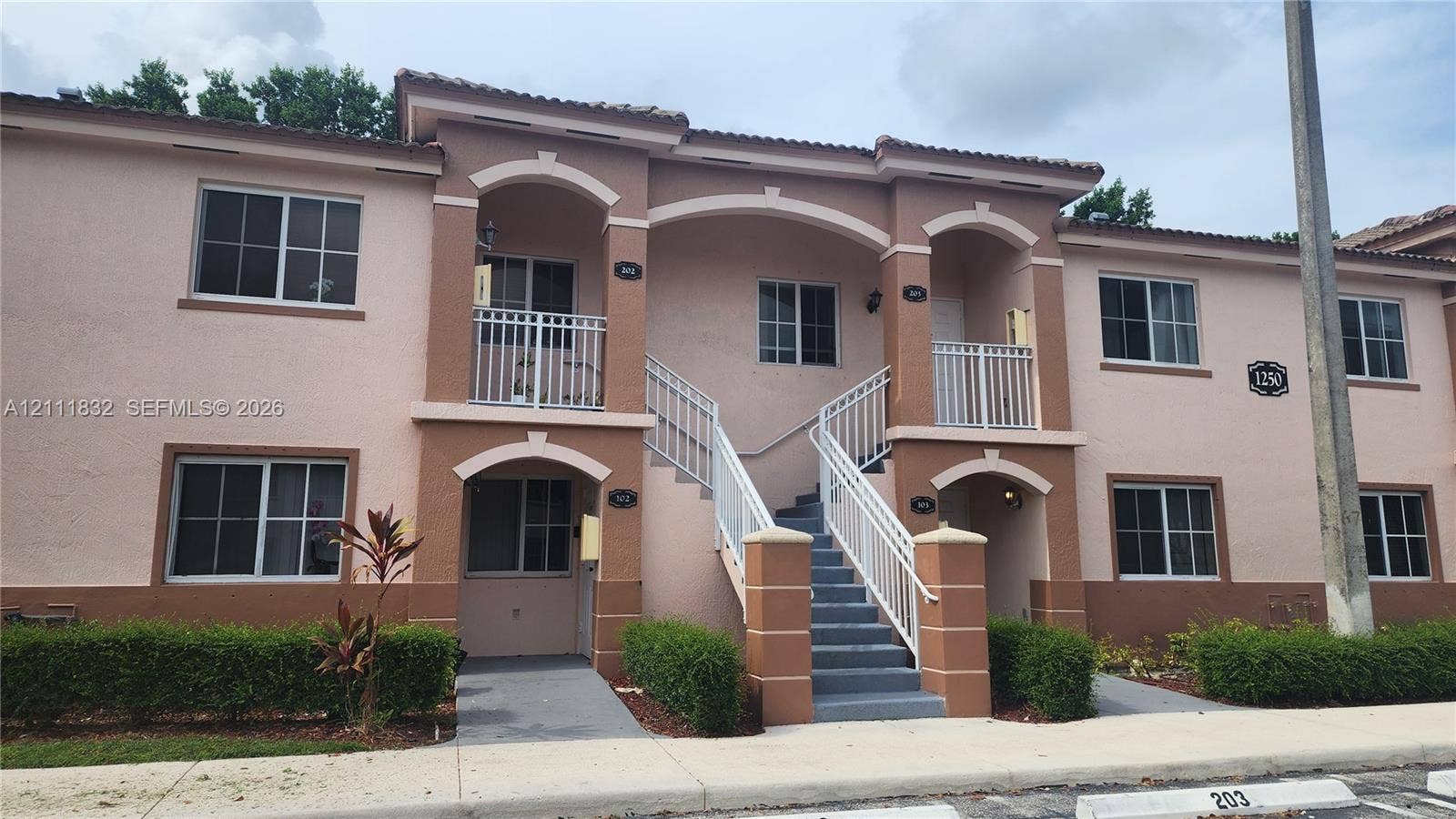 1250 SE 28th Court, #102, Homestead, FL 33035 Stucco exterior featuring arched entryways, concrete stairs with white metal railings, tiled roofline, and manicured shrubbery