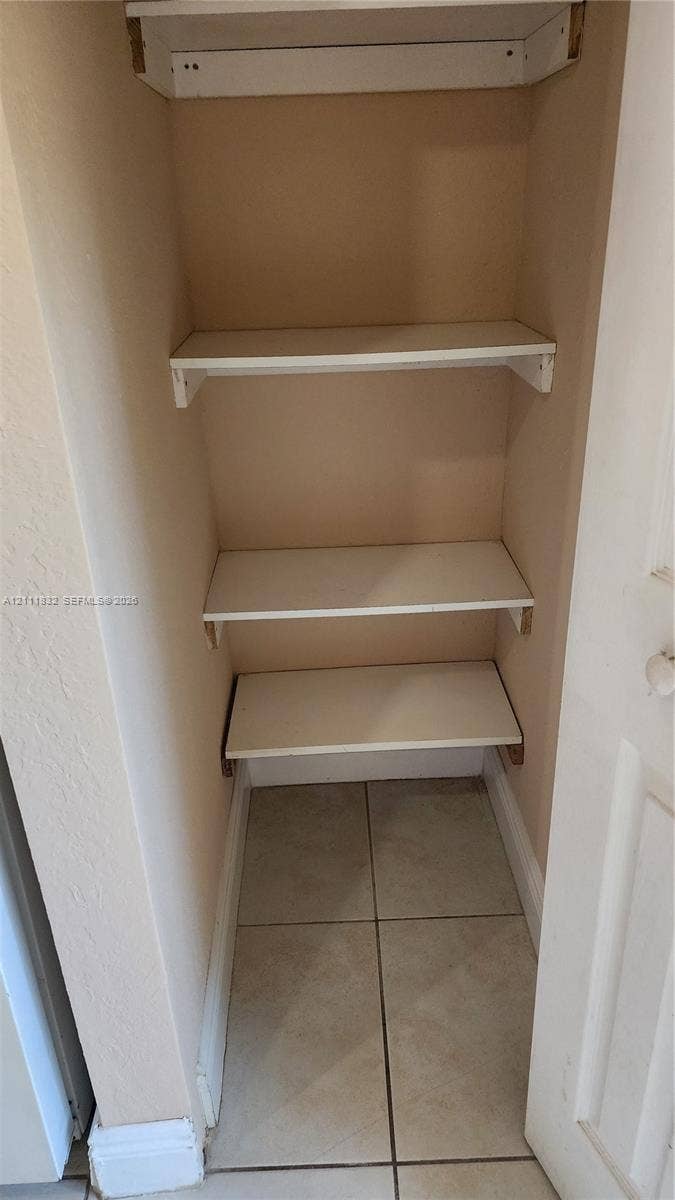 1250 SE 28th Court, #102, Homestead, FL 33035 Built-in storage closet featuring three white shelves and tiled flooring
