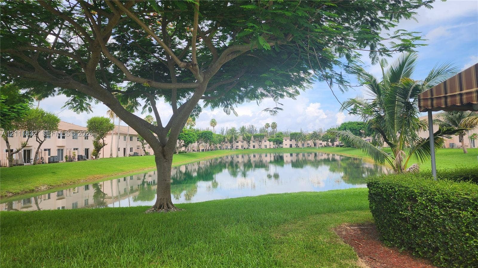 1250 SE 28th Court, #102, Homestead, FL 33035 Waterfront exterior featuring a central pond, manicured lawn, mature shade trees, and groomed shrubbery