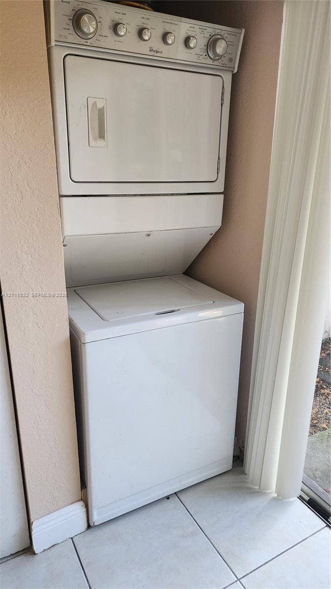 1250 SE 28th Court, #102, Homestead, FL 33035 White stacked laundry unit featuring a top-load washer and a control panel with tactile rotary dials, installed within a tiled-floor alcove